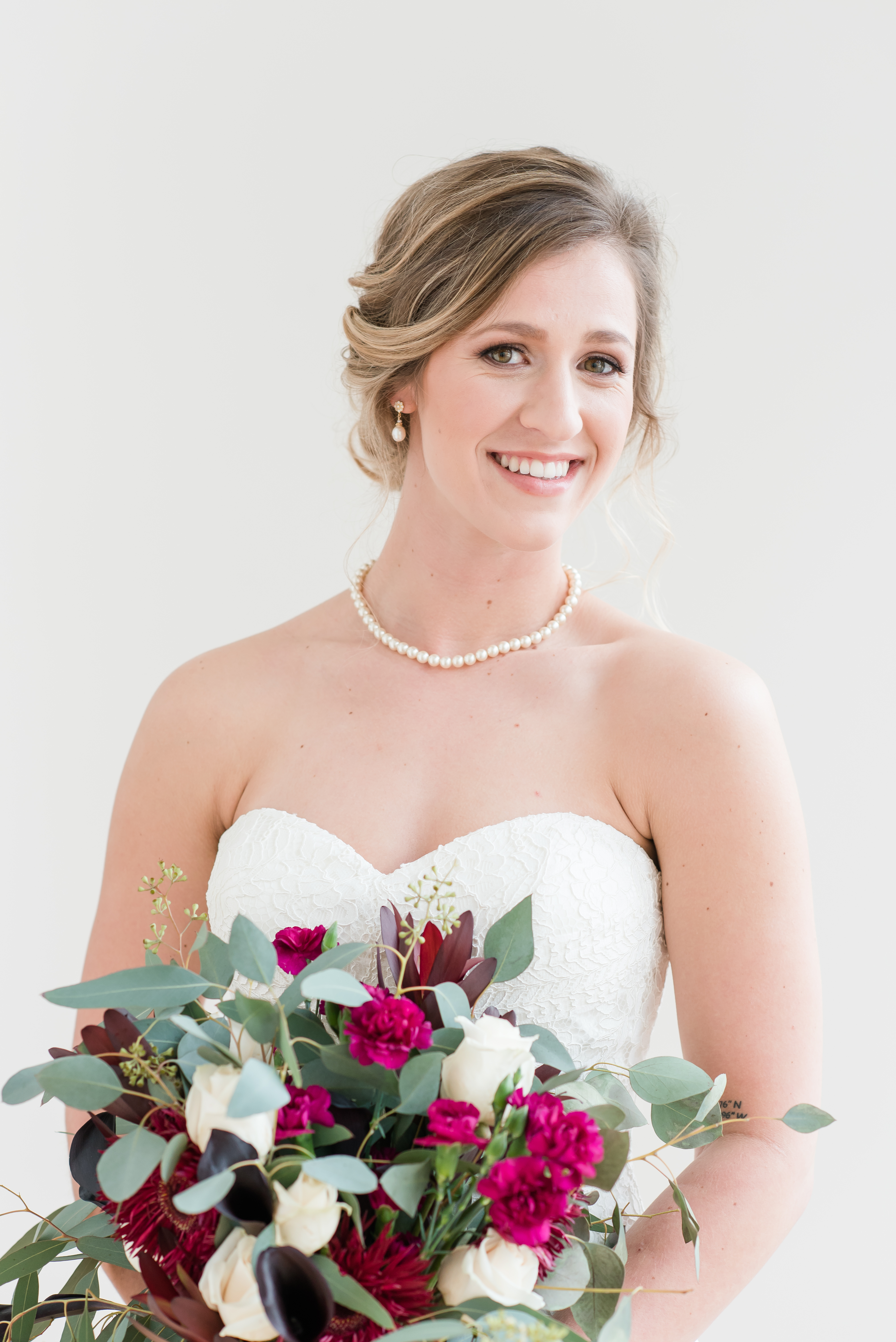 Bride looking at camera with red and green flowers at the Glass Box