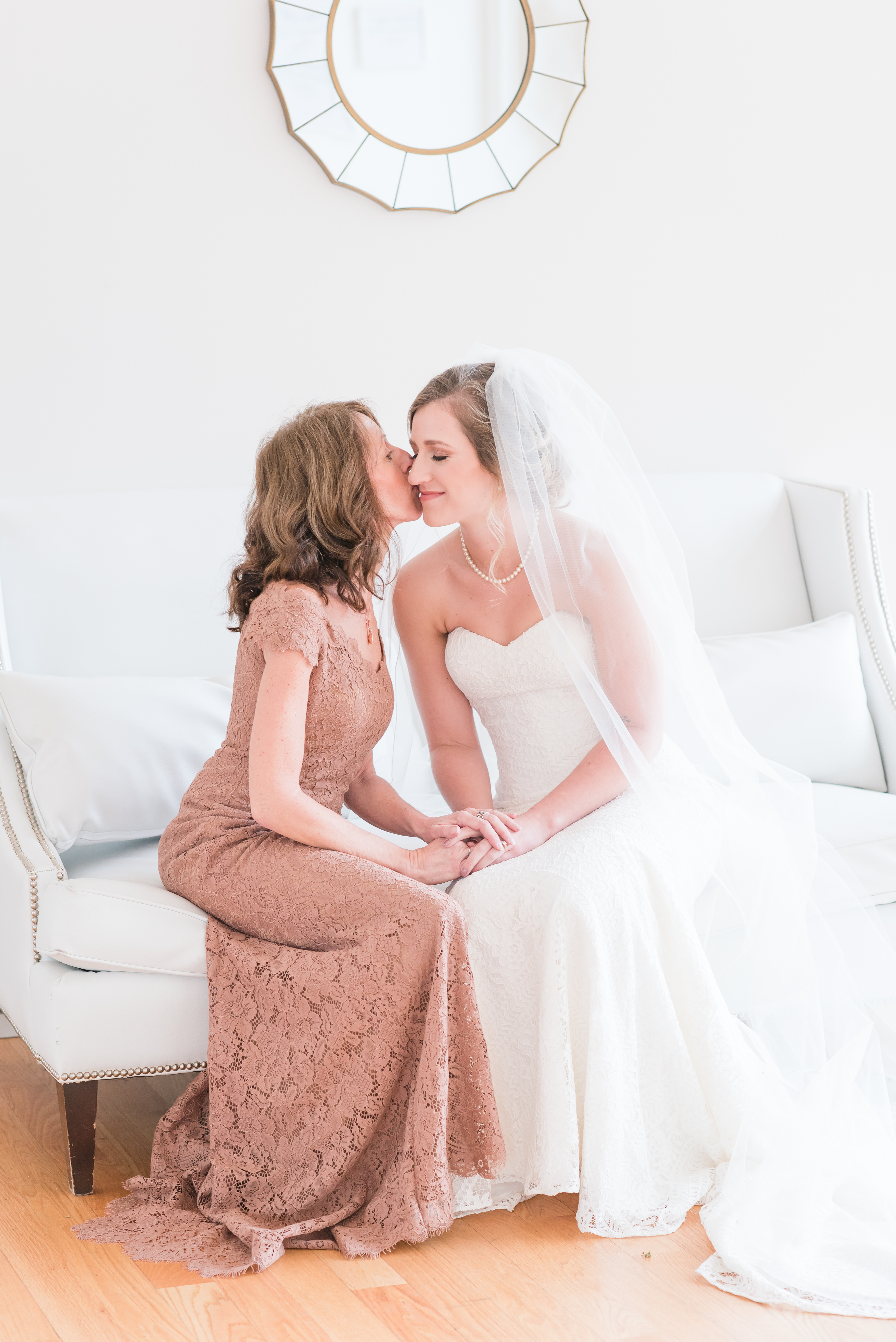 Mother of the bride kissing the bride on the couch at the Glass Box