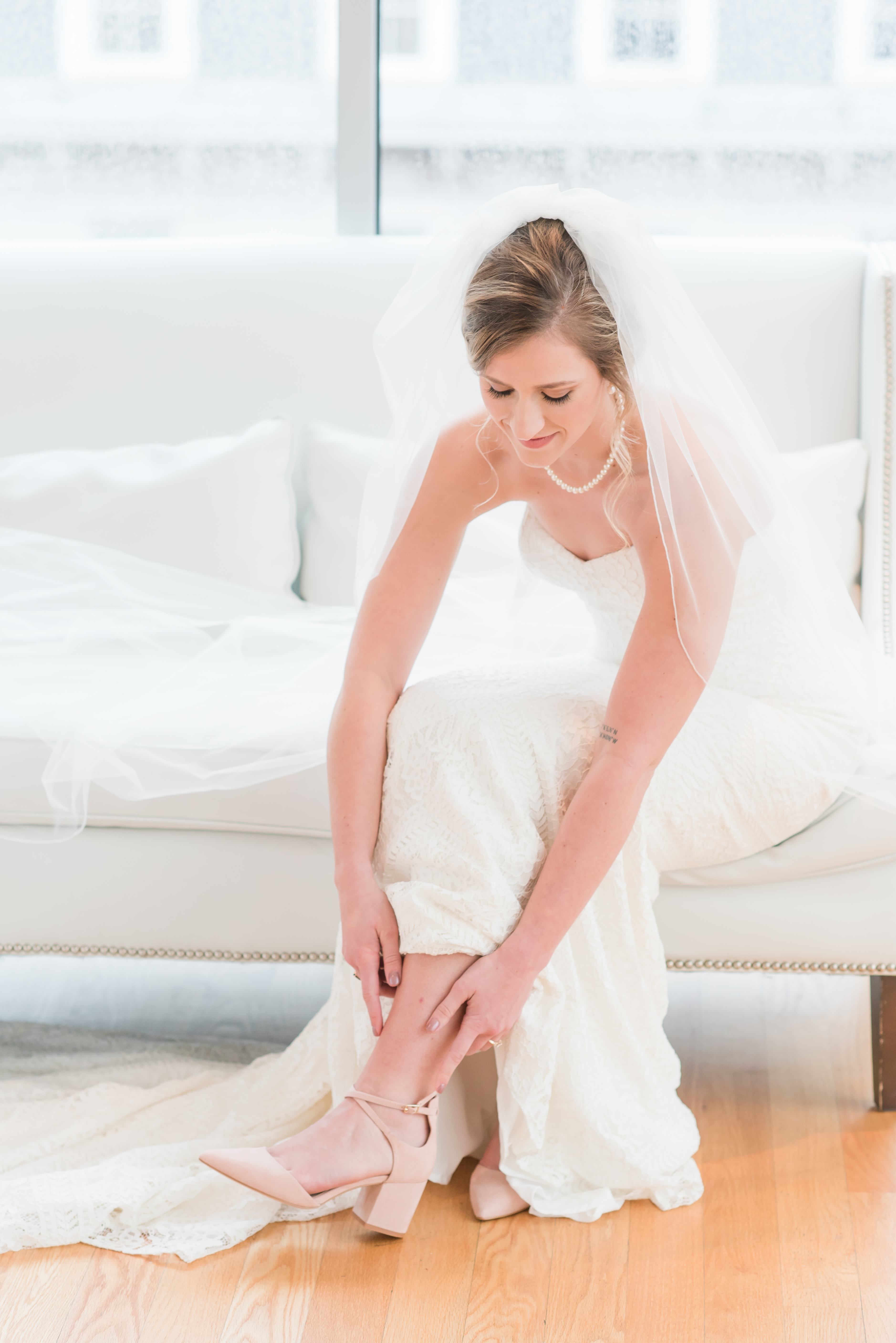 bride fixing wedding heels sitting on the couch with cathedral length veil at the Glass Box