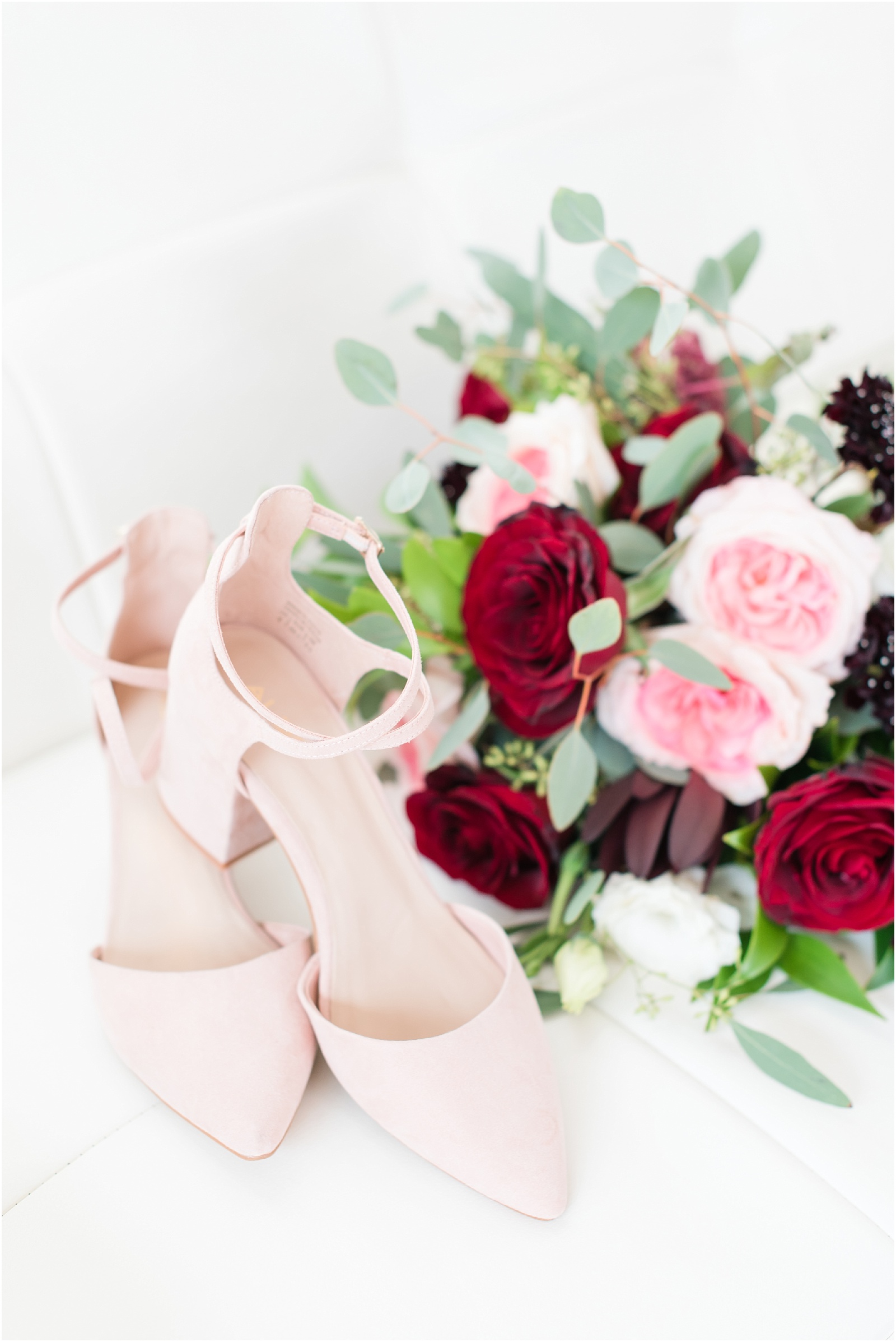 Brides pink suede shoes with Brides Boquet filled with pink and red rosses with gray green greenery at the glass box
