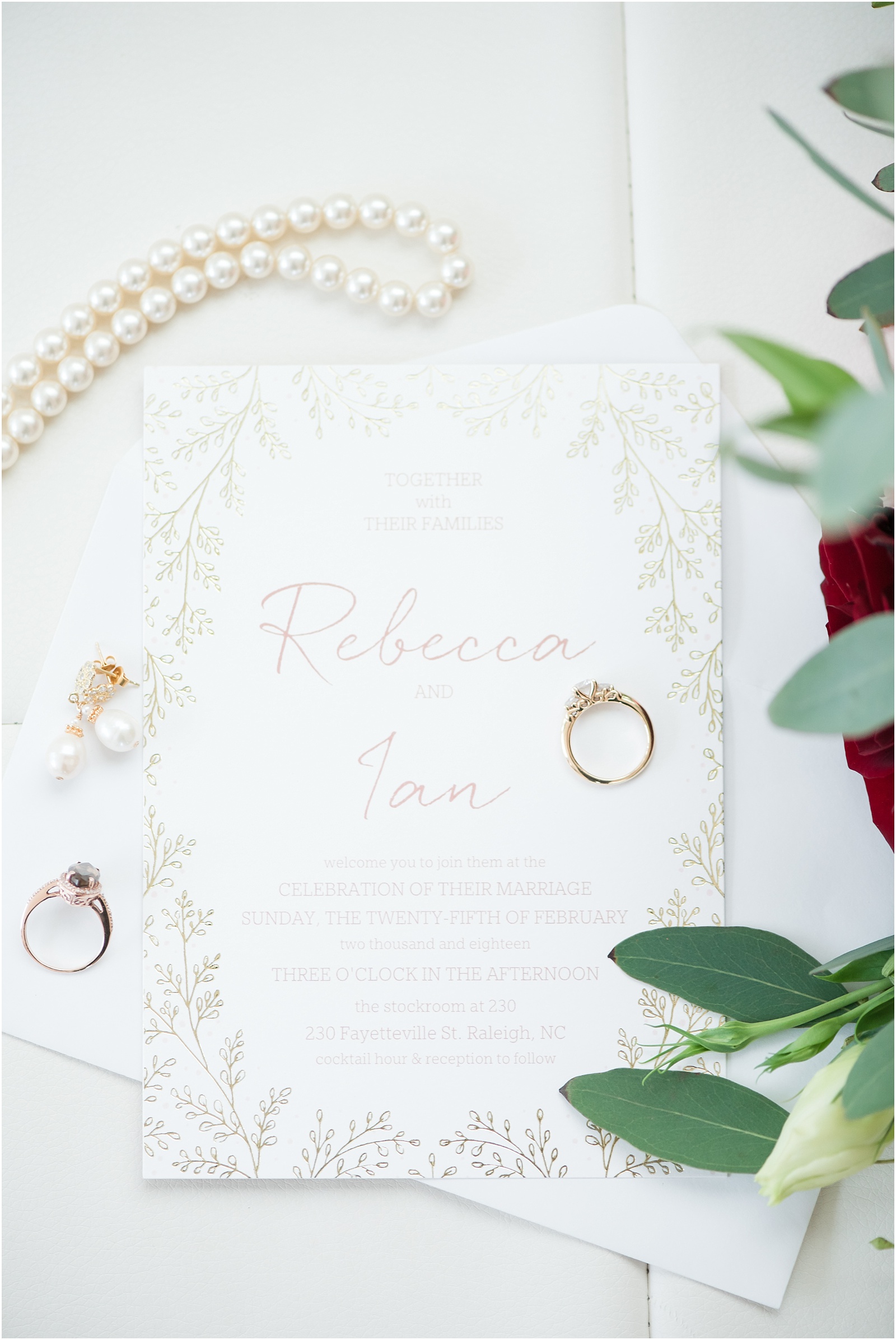 Wedding invitation with soft pastel writing, with perals, wedding rings boquet with greenery and red and white flowers at the glass box