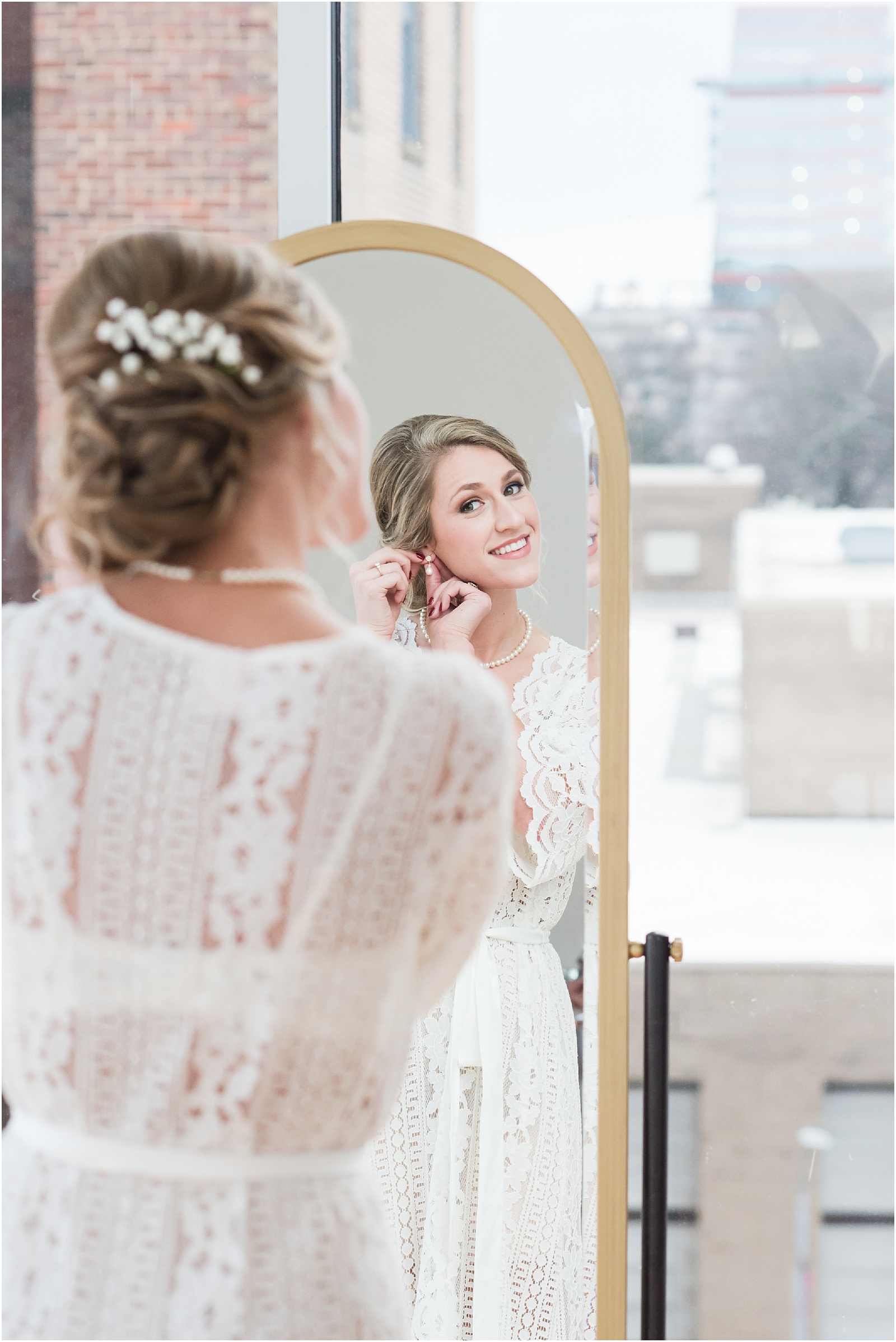 Bride adjusting earings looking into mirror at the glass box