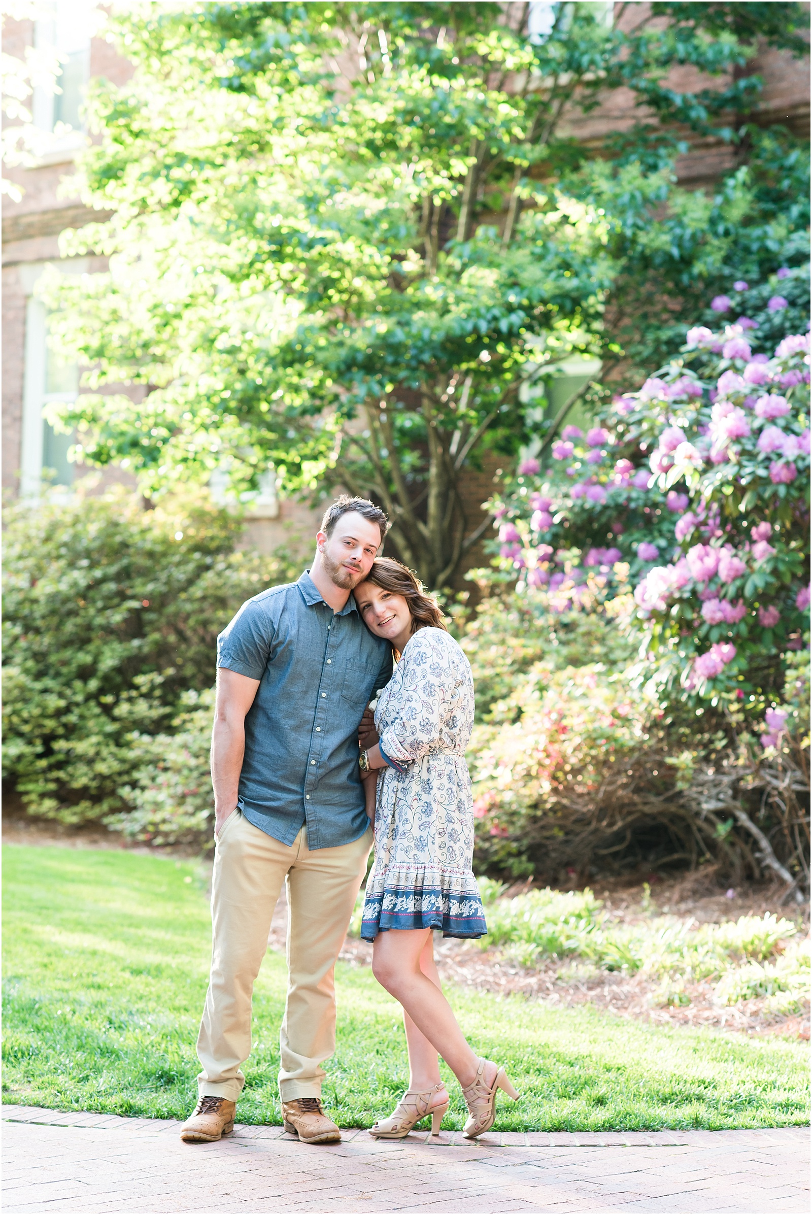 young couple cuddling looking at camera in front of hydrangea bush at Elon College