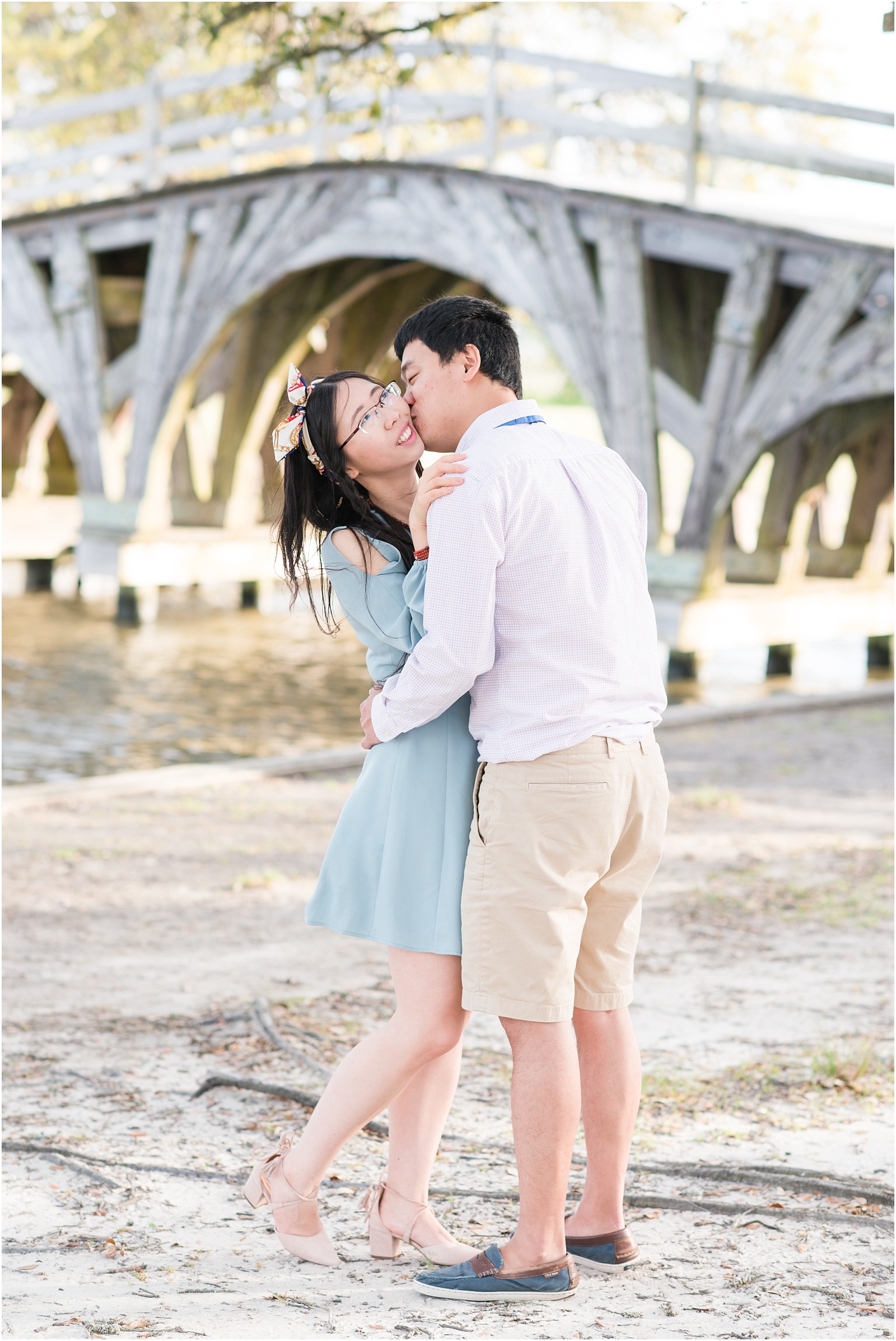 young couple kissing in front of bridge at Whalehead Club