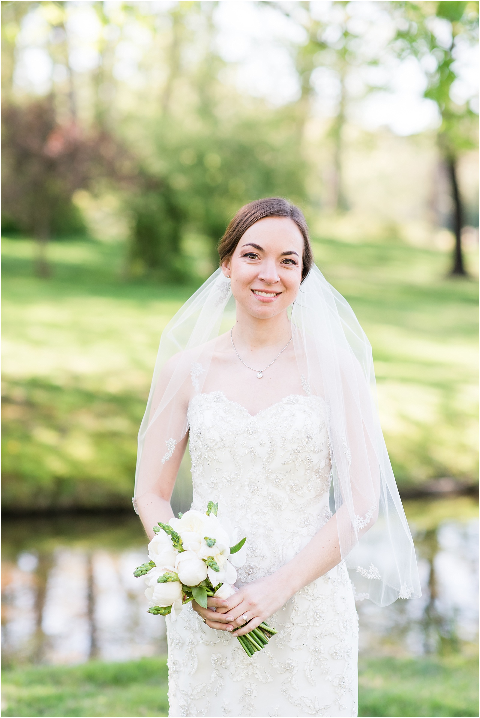 bride standing in front of pond outside holding wedding bouquet with veil at a Home Estate bridal session