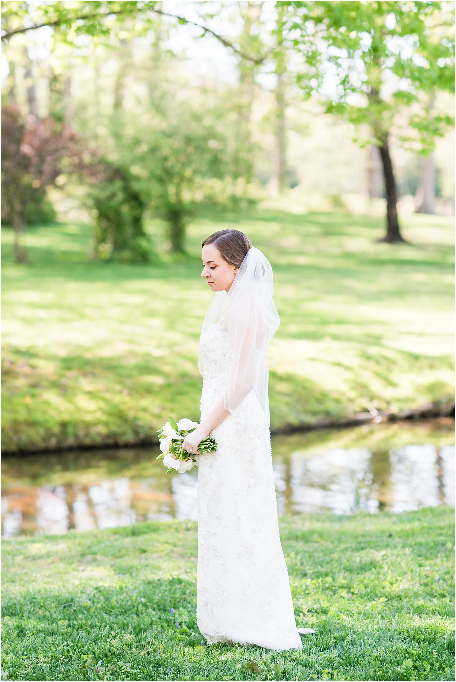 bride standing in front of pond looking down holding white and green wedding bouquet outside at a Home Estate bridal session