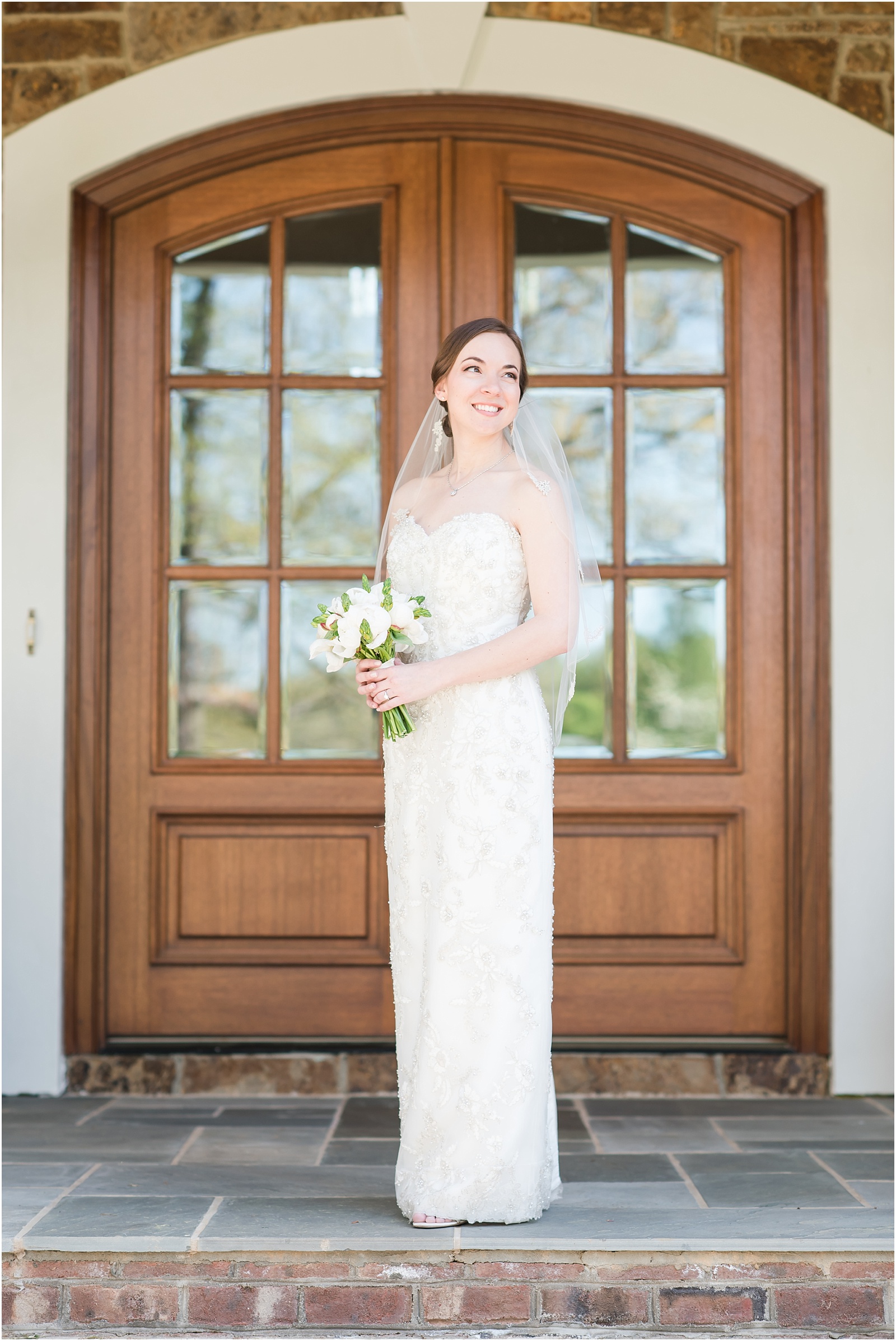 bride standing on front porch looking up holding a white and green bridal bouquet at a Home Estate