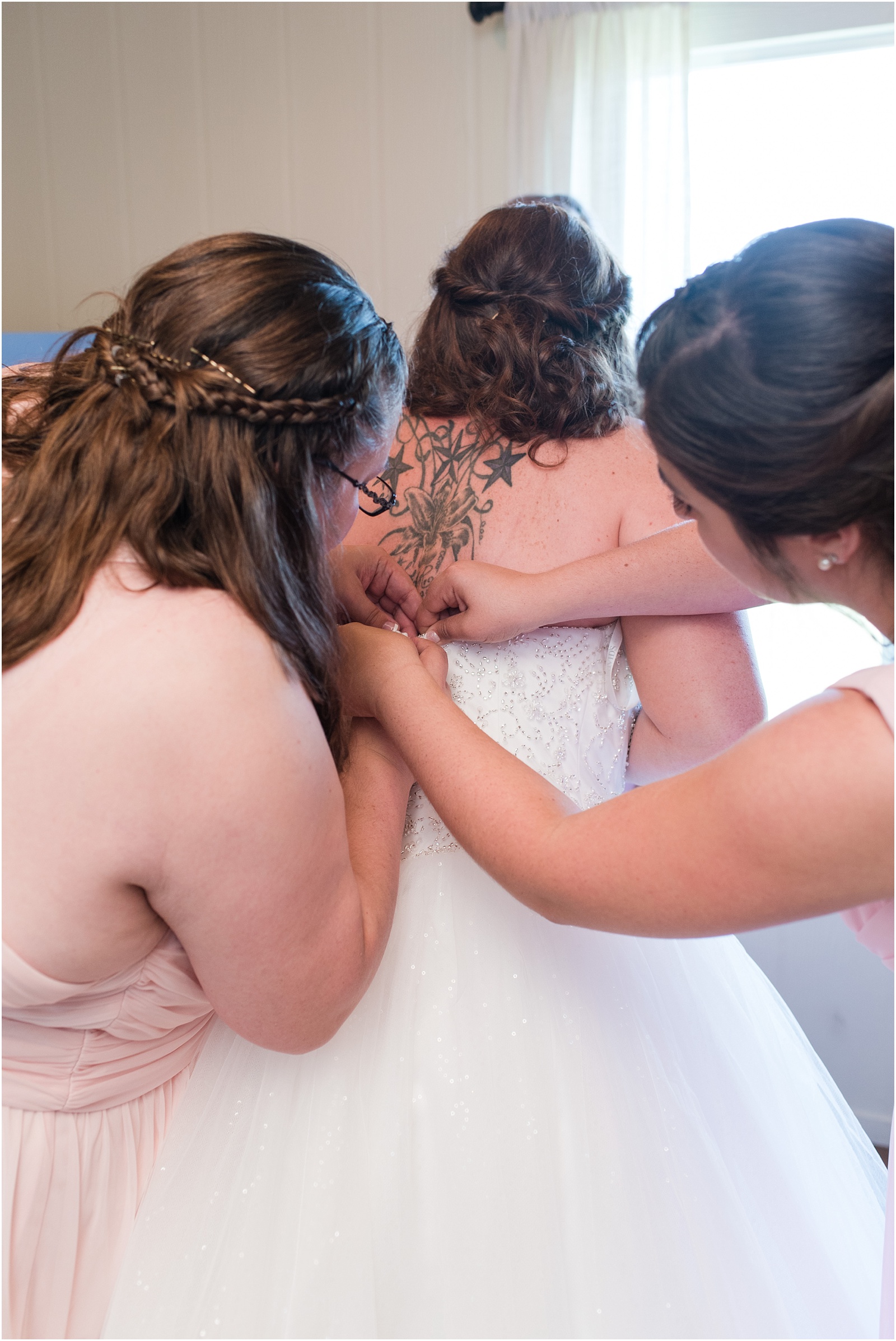 bridesmaids zipping up bride into her wedding gown at Starlight Meadow