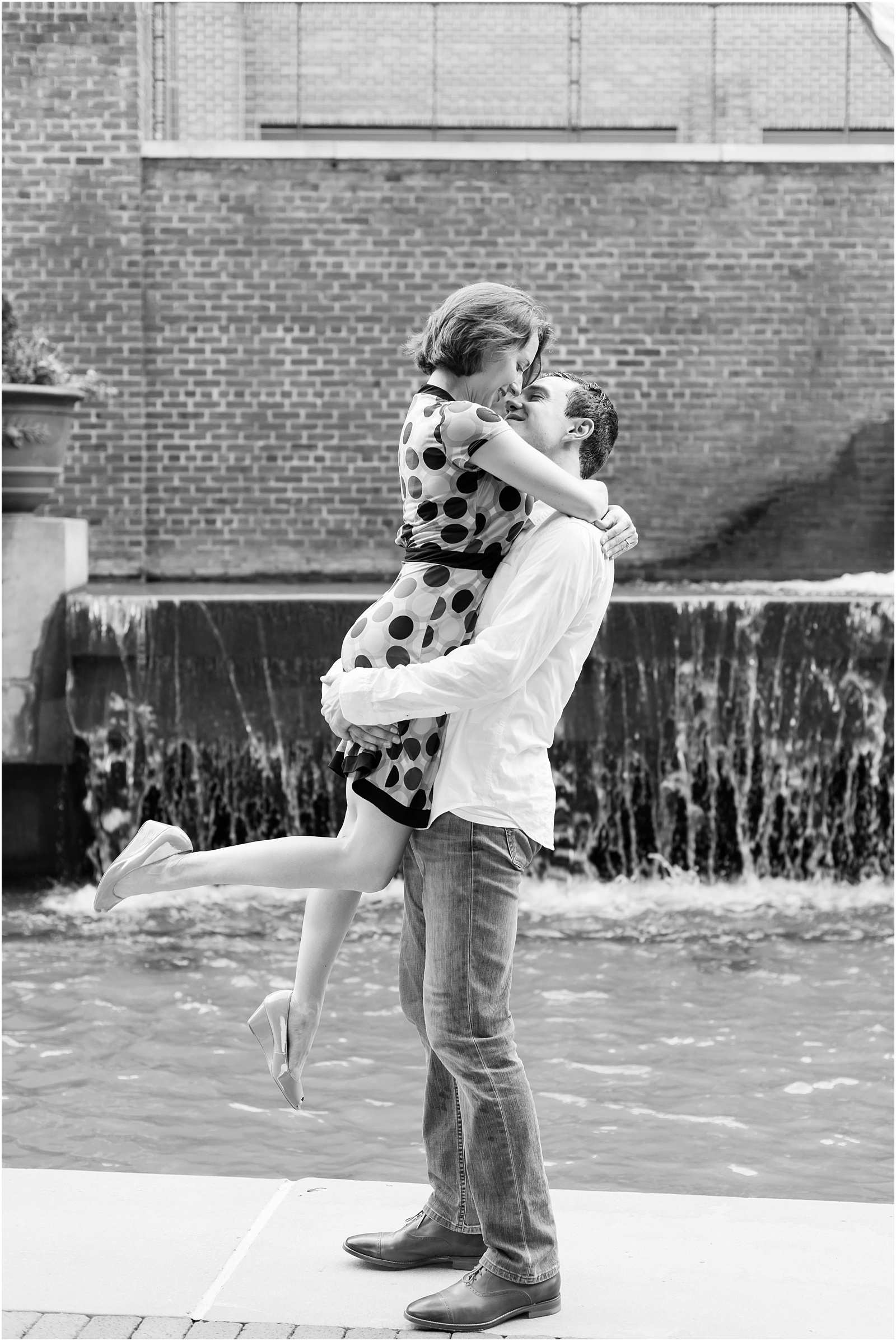 young man lifting up young woman in front of waterfall almost kissing at the American Tobacco Campus