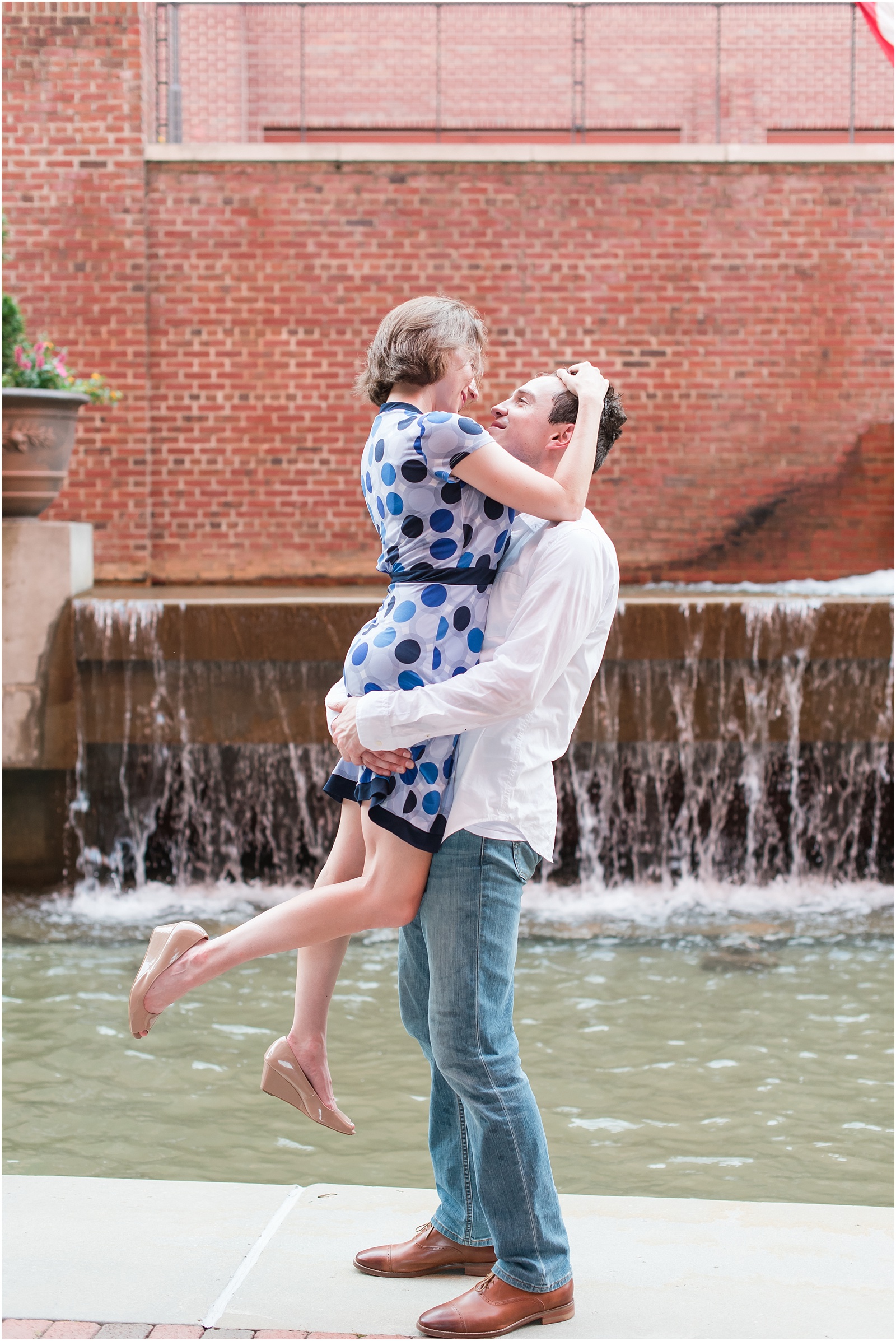young man lifting young woman in front of the waterfall at the American Tobacco Campus