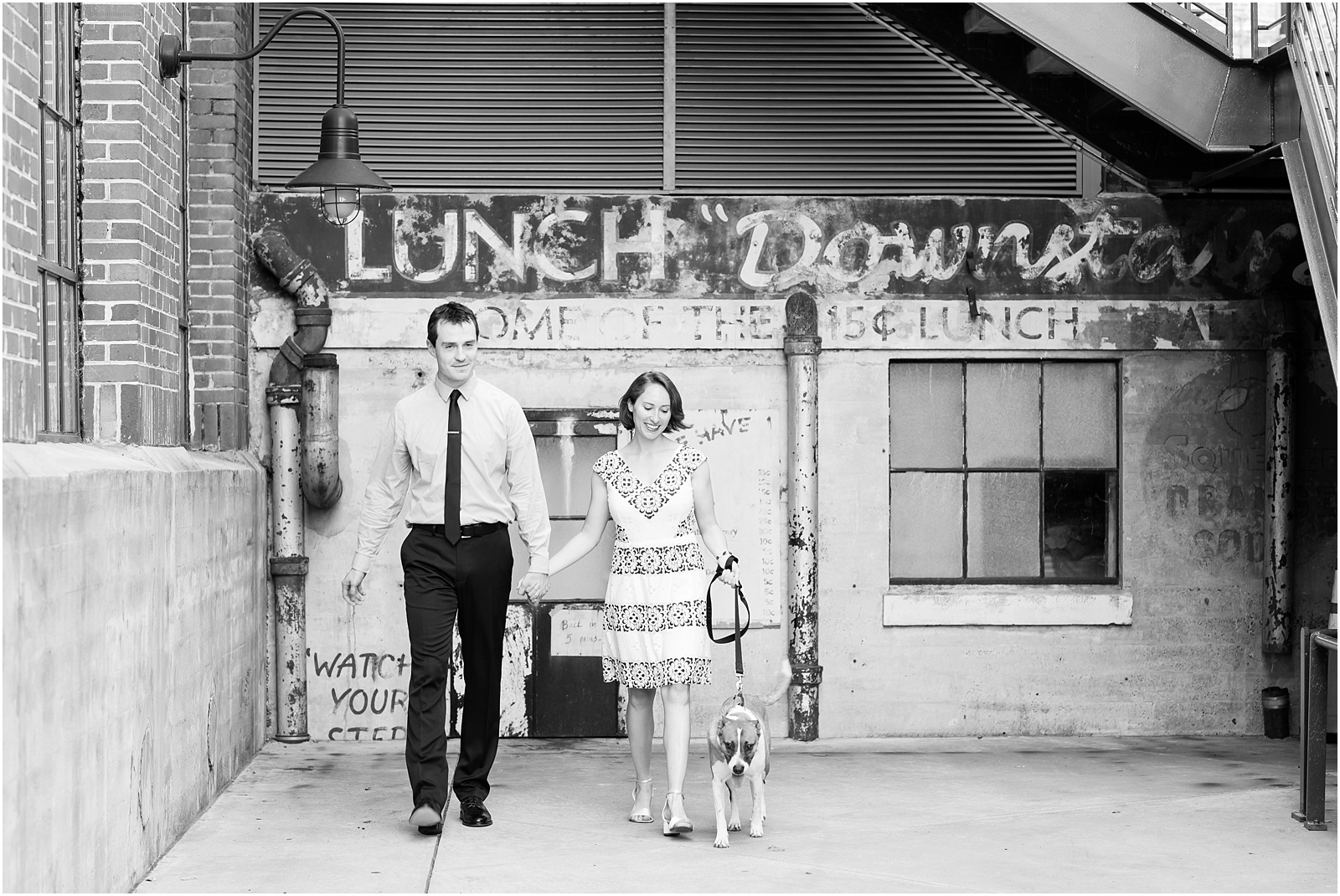young couple walking with dog in front of rustic wall at the American Tobacco Campus
