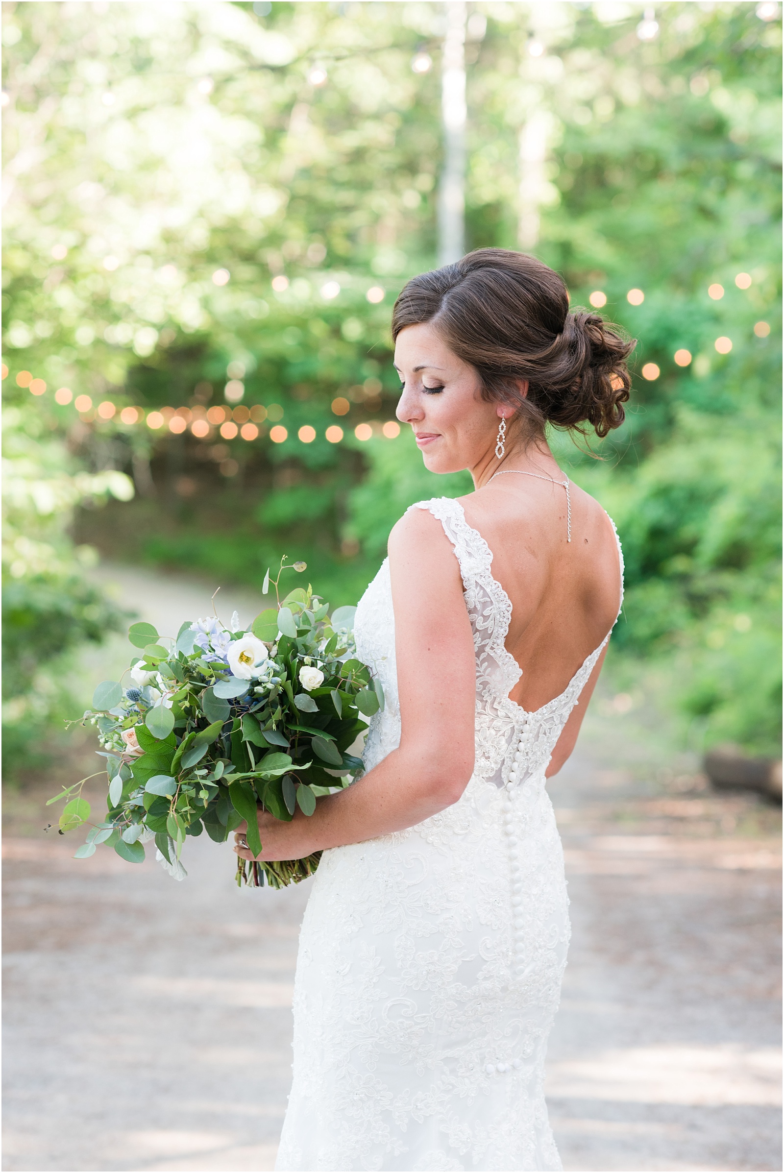 bride smiling while looking down holding lush green and white bridal bouquet at The Meadows At Walnut Cove Bridal Session