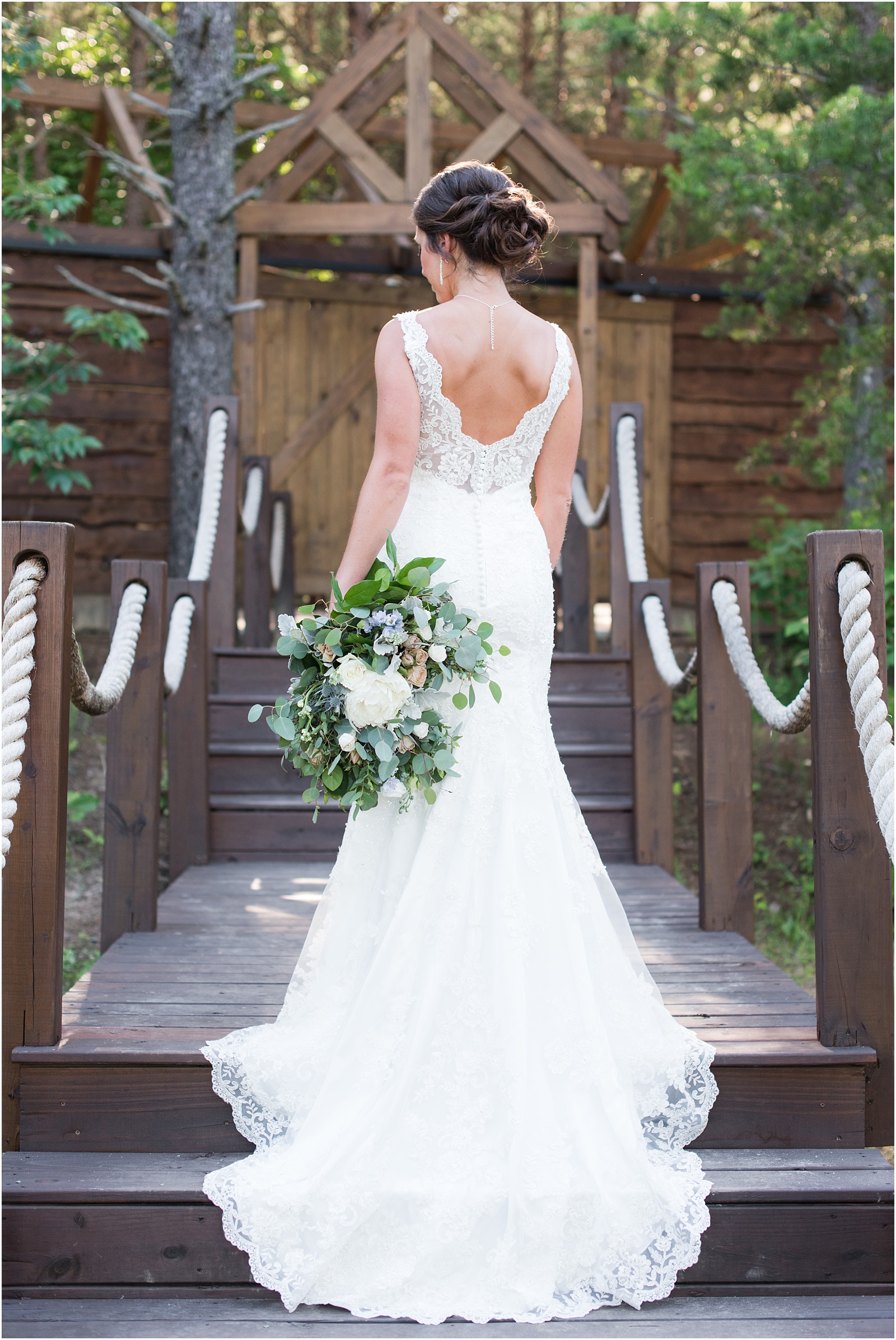 the back of the brides dress holding lush green bridal bouquet on stairs at The Meadows At Walnut Cove