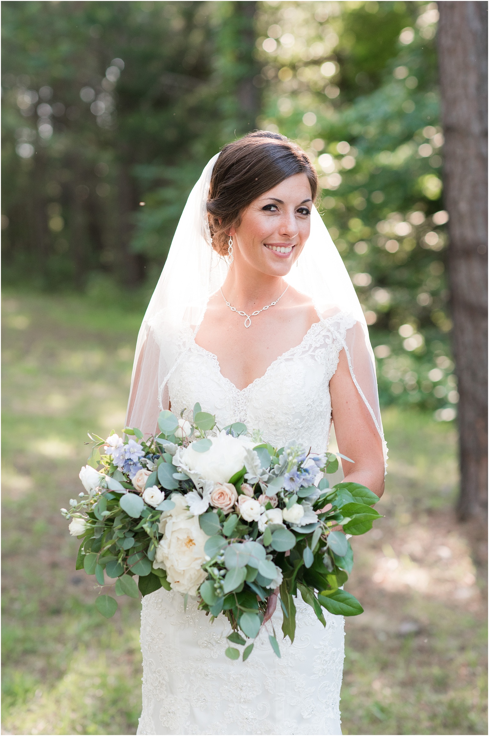 bride looking at camera with the sun glowing behind her holding a big lush bridal bouquet at The Meadows At Walnut Cove