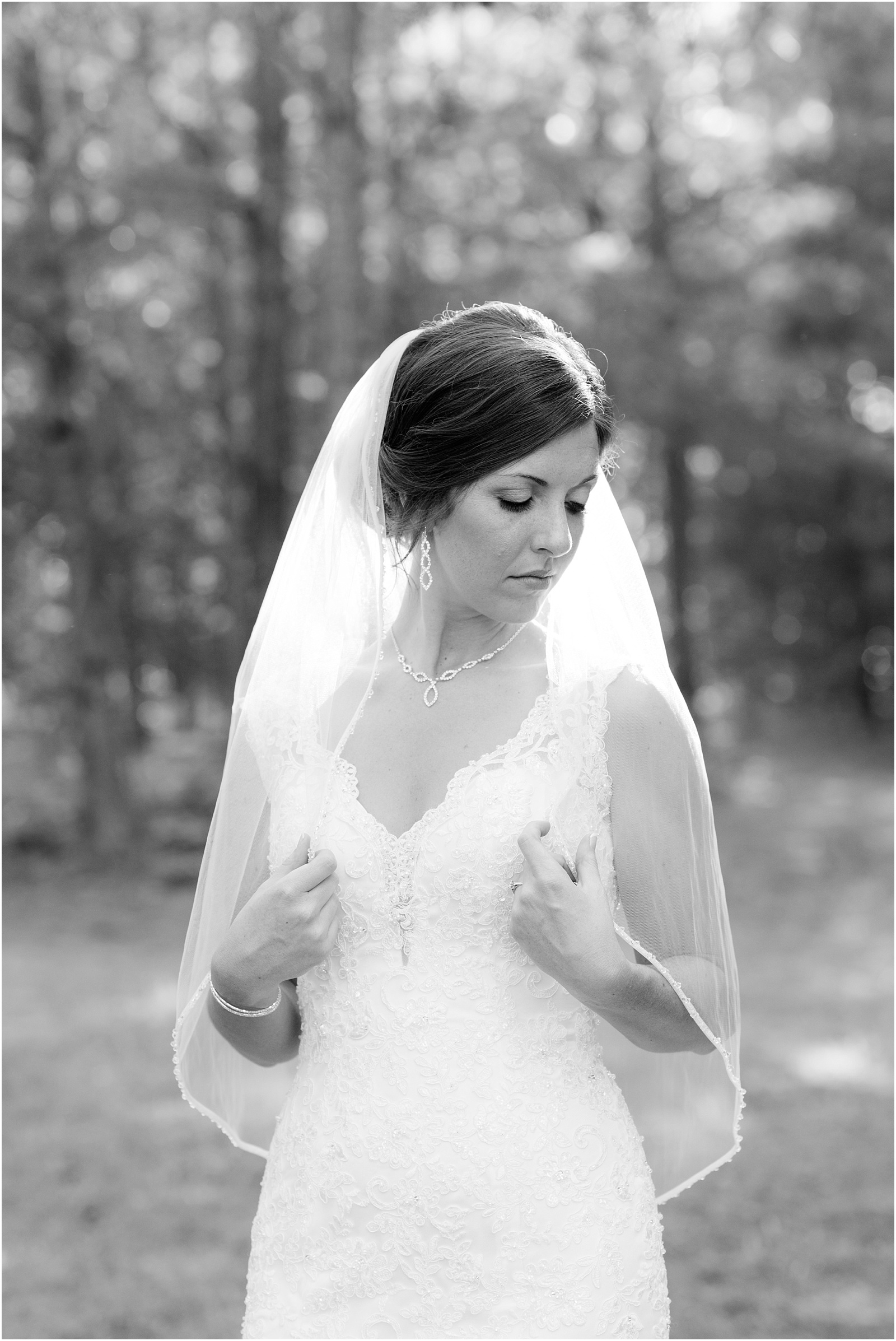 bride looking down at shoulder holding veil in hands black and white at The Meadows At Walnut Cove