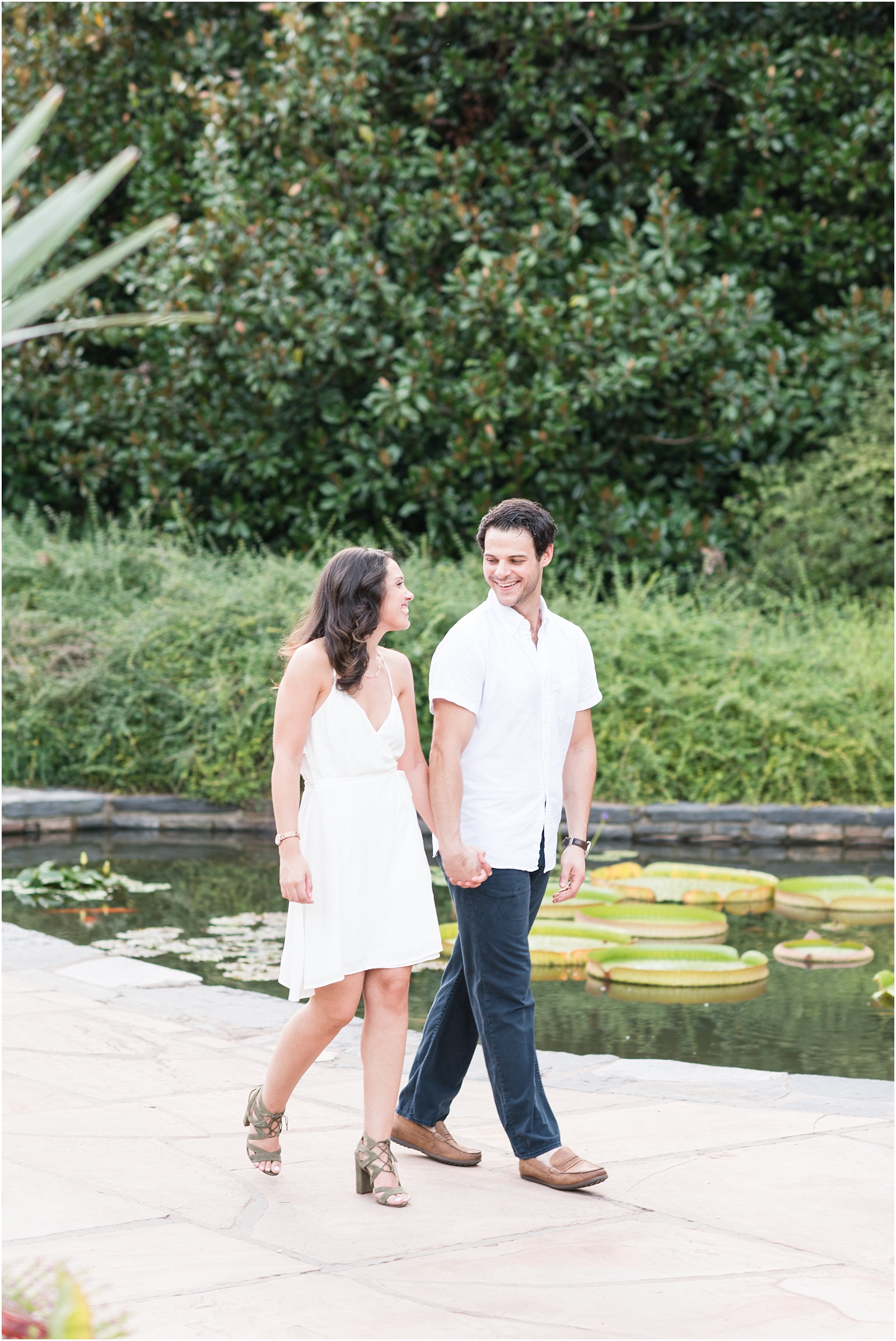 groom in white button up shirt and blue jeans walking hand in hand with bride wearing white dress walking in front of koi pond at Sarah P Duke Gardens