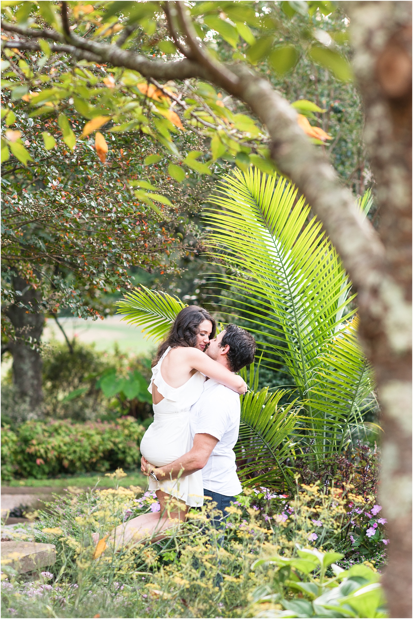 man wearing white button shirt lifting up bride wearing white dress almost kissing at Sarah P Duke Gardens