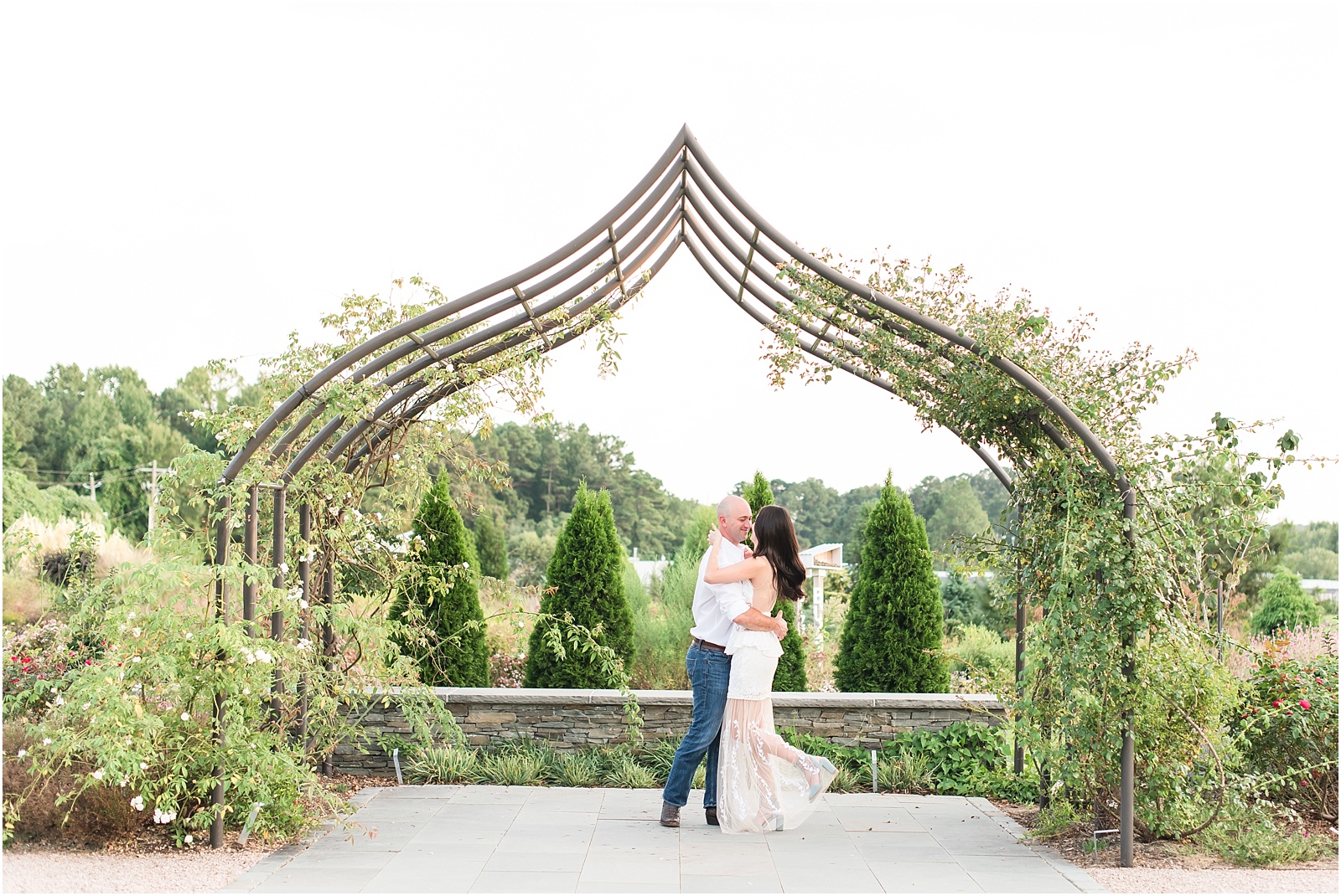 man wearing a white shirt and woman wearing a white dress twirlling underneath a vine arbor at JC Raulston Arboretum