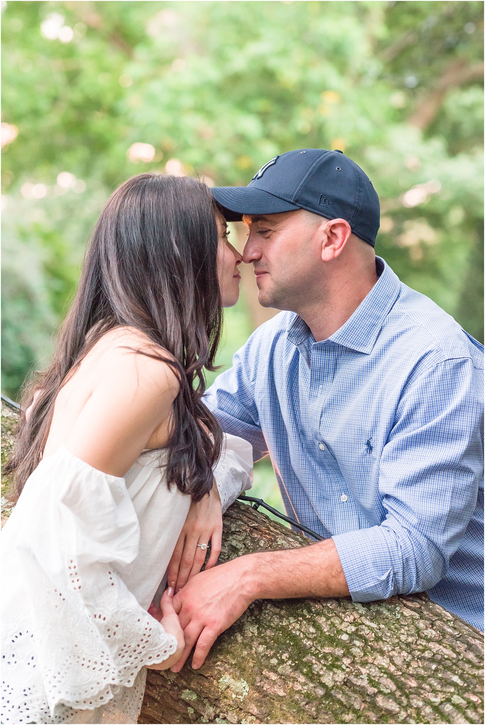 a man wearing a blue checked button up shirt giving butterfly kisses to a woman wearing a white blouse across a oak tree at JC Raulston Arboretum