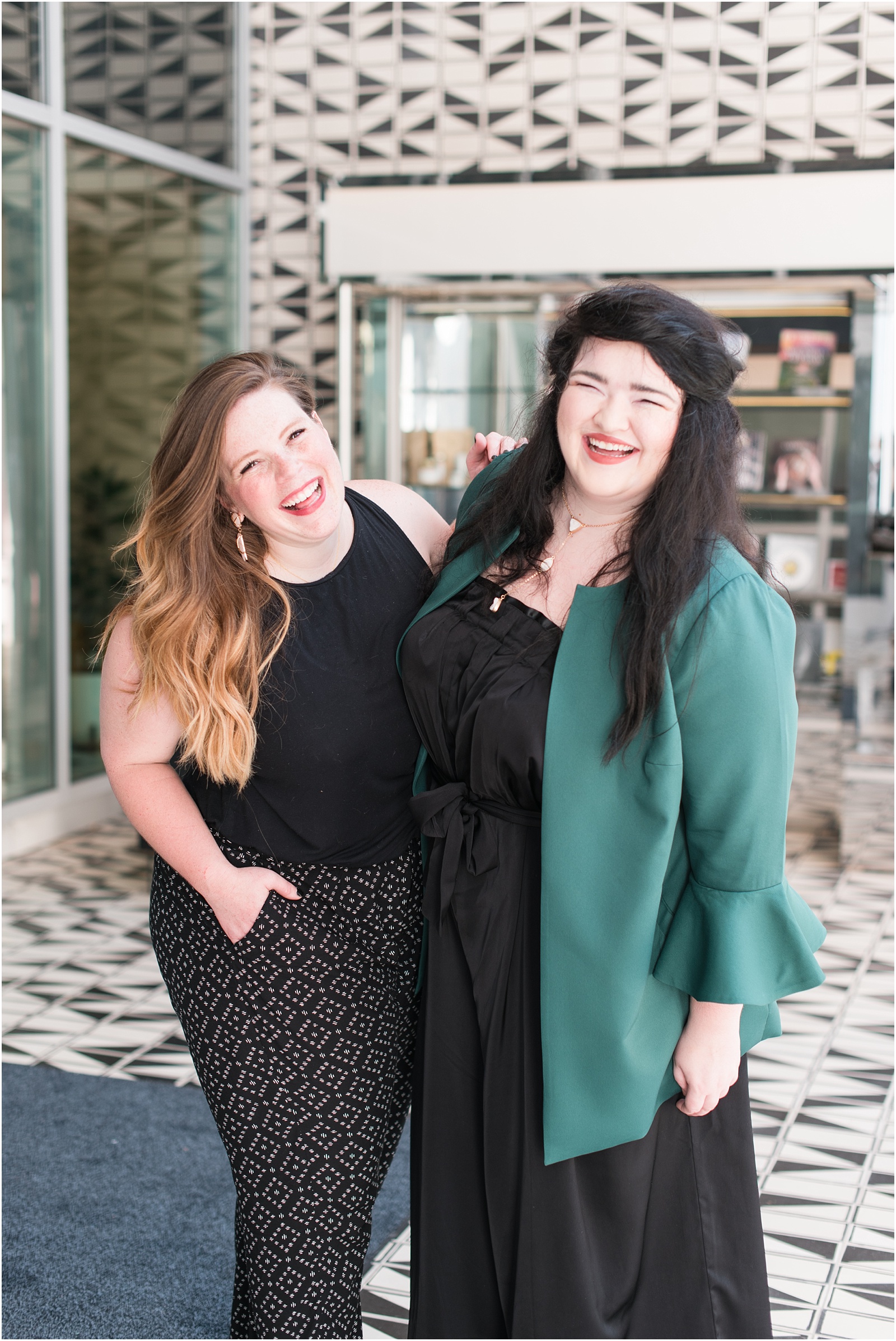 two ladies laughing against white brick background wearing black and green at the Durham Hotel