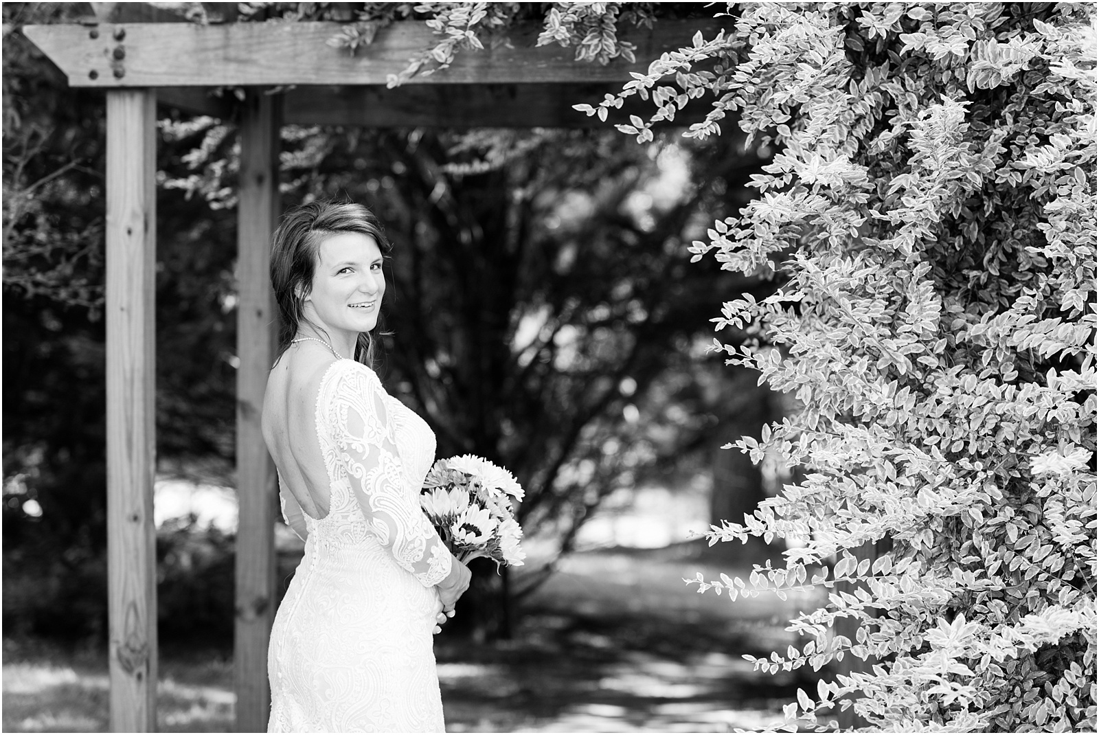 black and white with bride looking at the camera standing in front of arbor