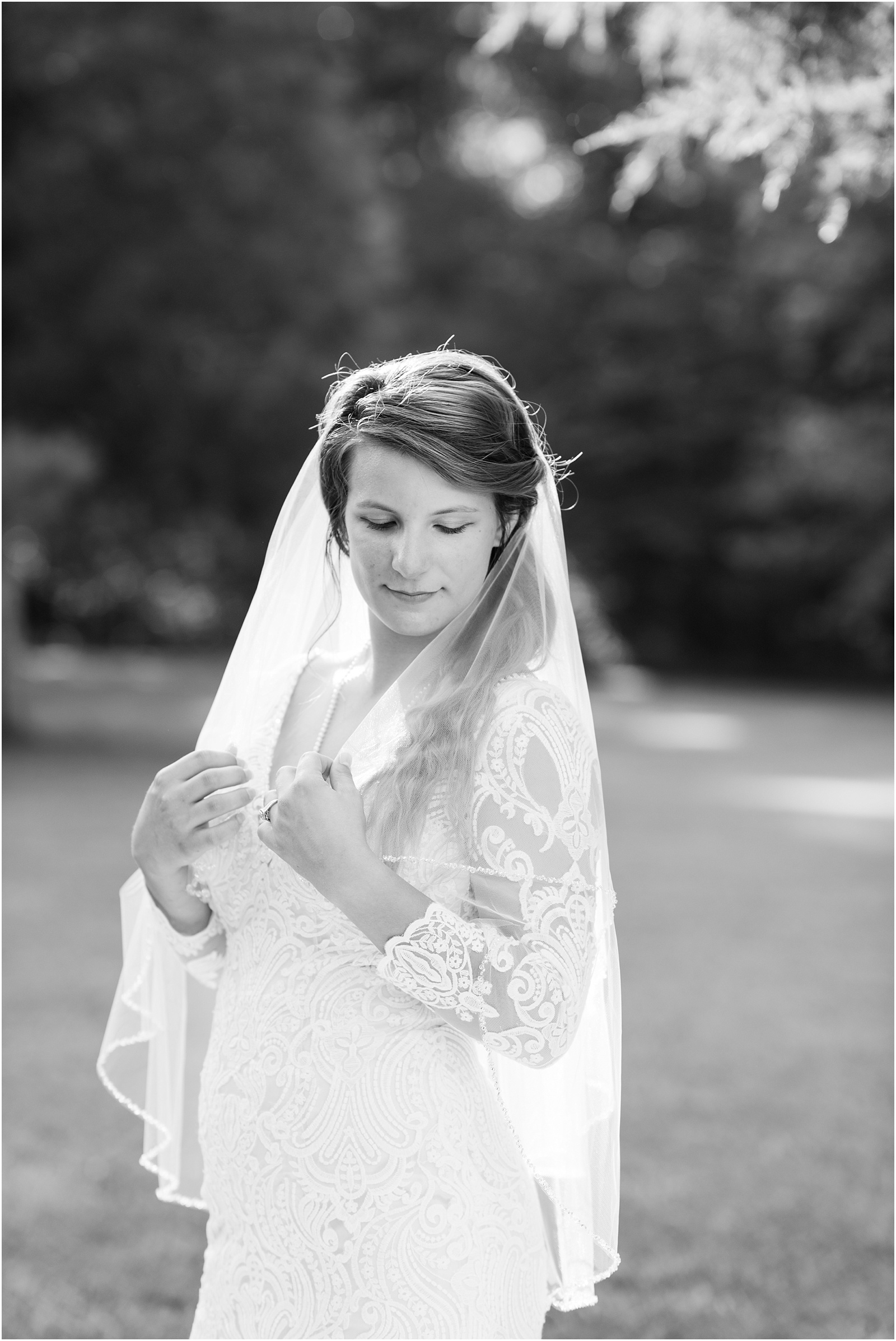 black and white of bride looking down while holding onto her veil