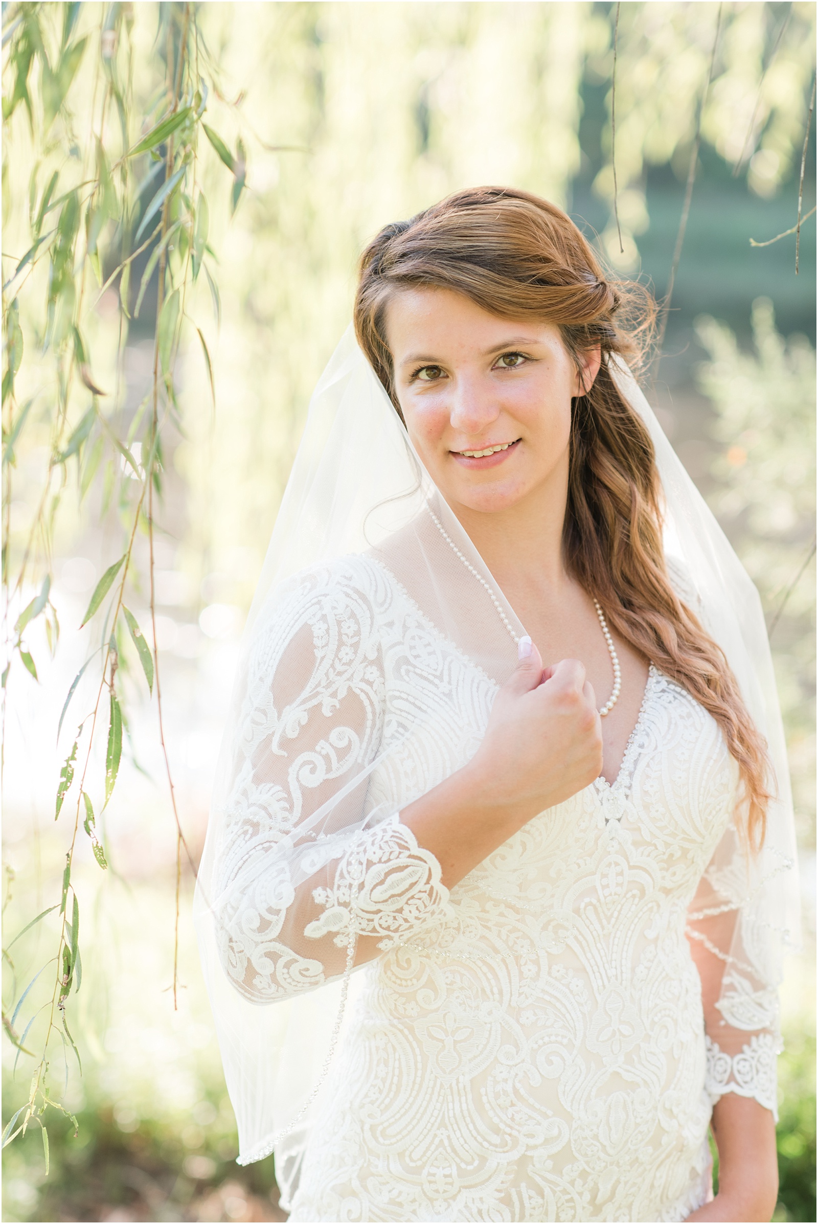 bride holding on to her veil while looking at the camera under willow tree
