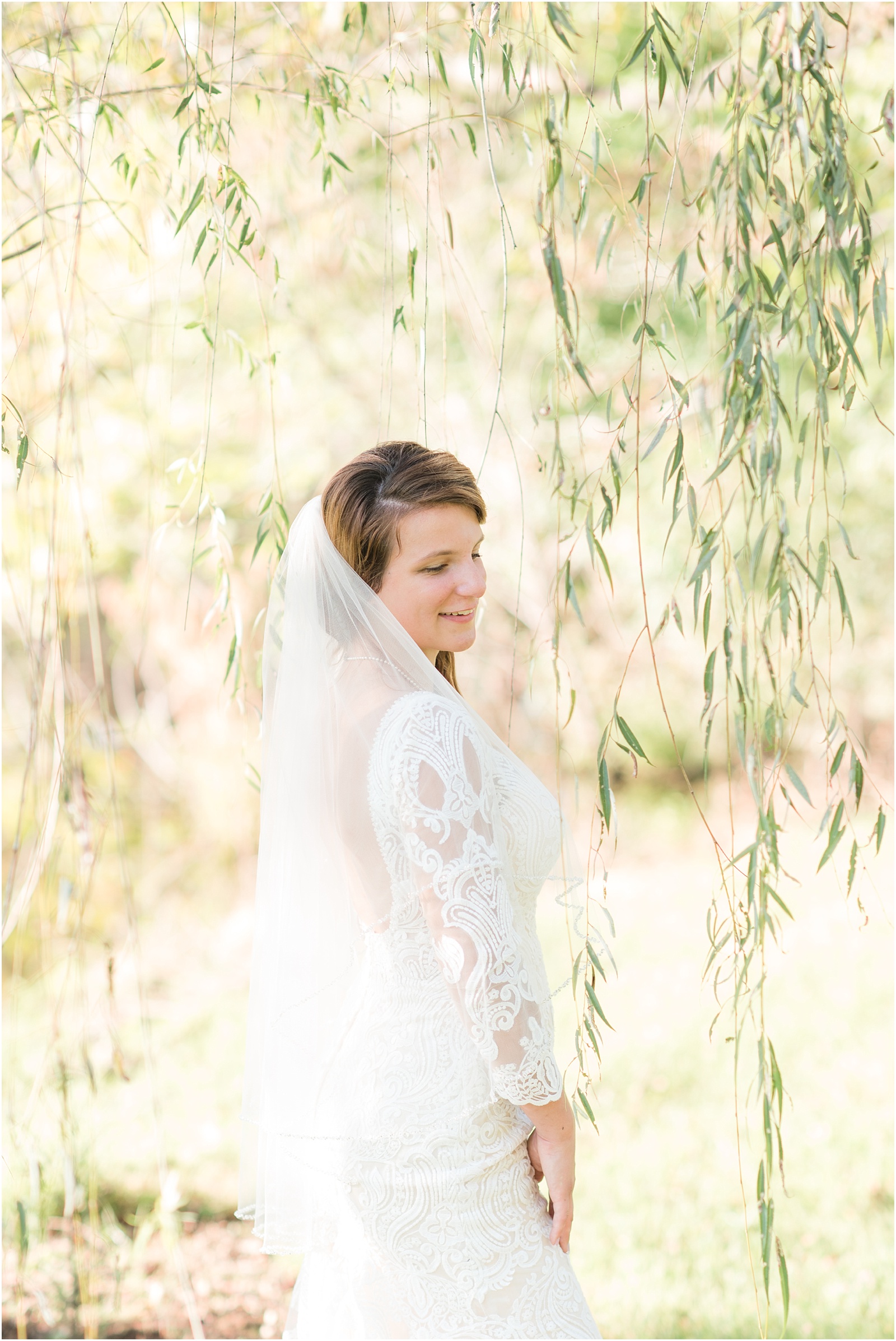 bride looking down wearing a chamange colored dress wearing a veil under a willow tree