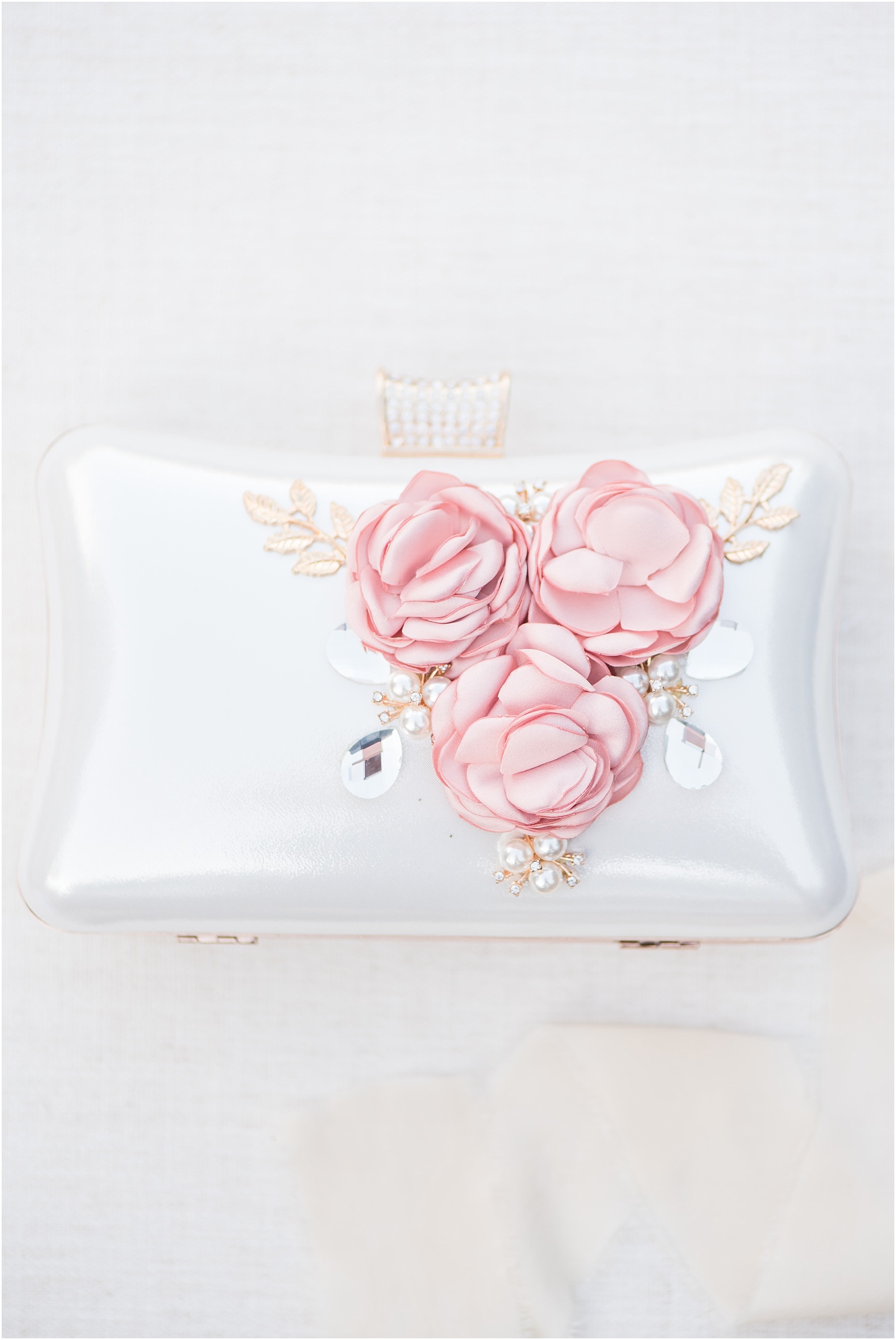 a white clutch with gold detailing and pink flowers