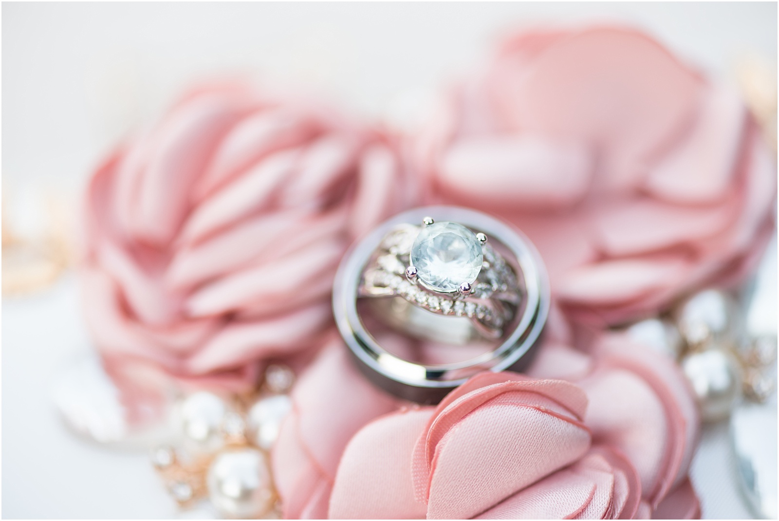 a blue stoned sliver engagement and wedding band set sitting in a sliver wedding band on top of pink flowers on a clutch