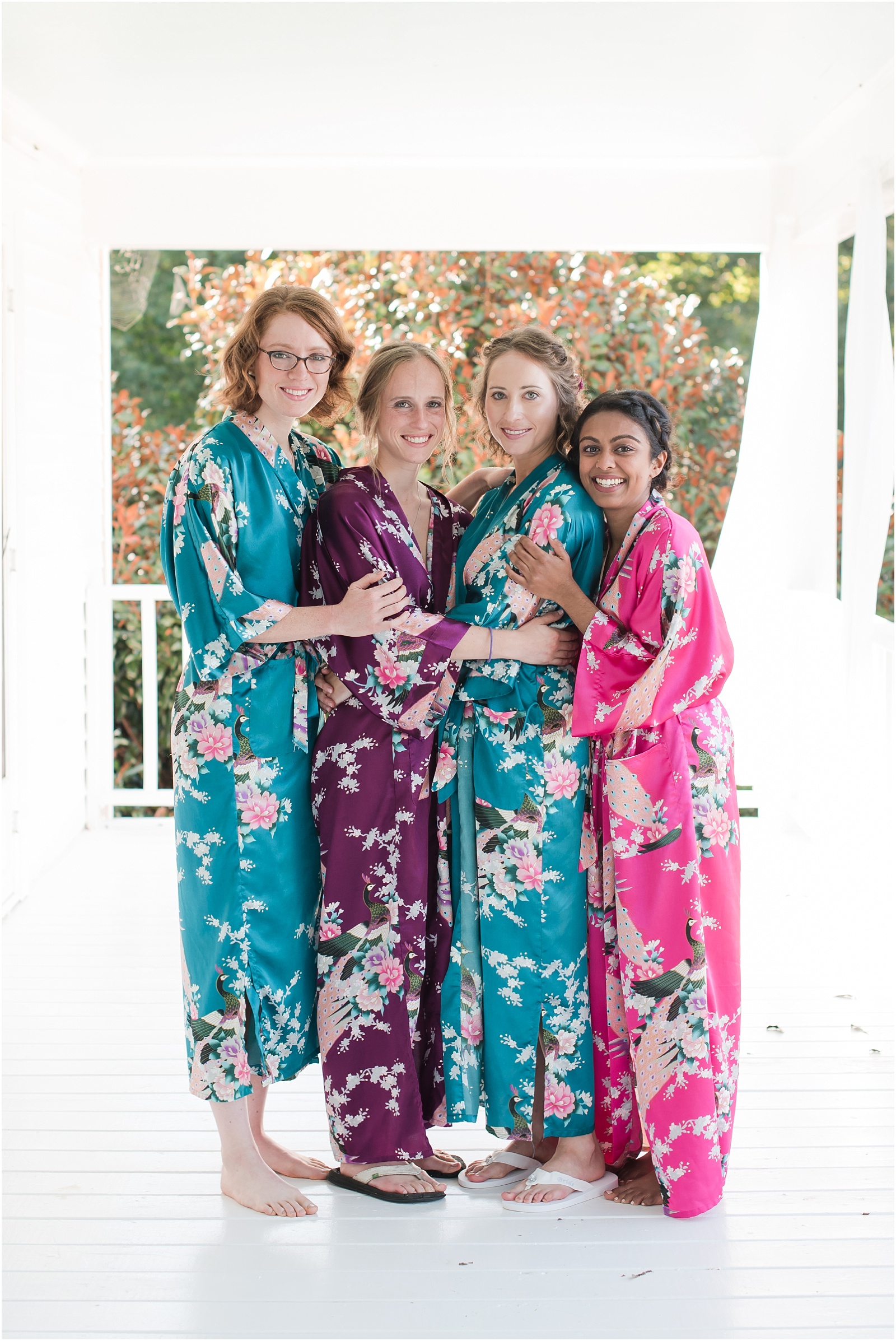 bridesmaids wearing bridal robes hugging the bride wearing a bridal robe on the porch of Merry Hill Weddings