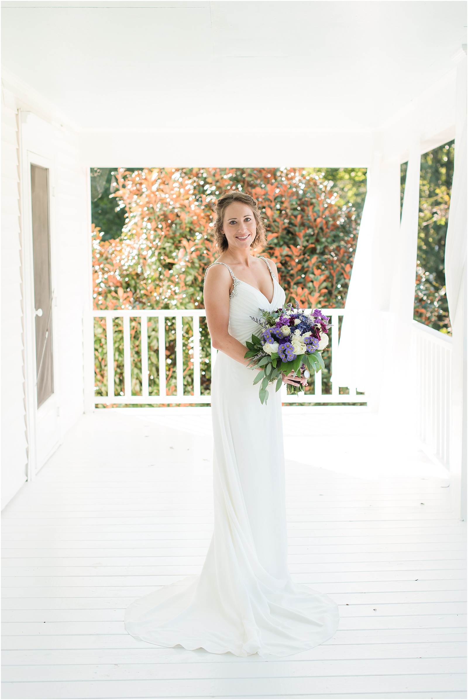 bride wearing white dress with sliver beaded straps holding a purple/pink/green wedding bouquet on the porch of Merry Hill