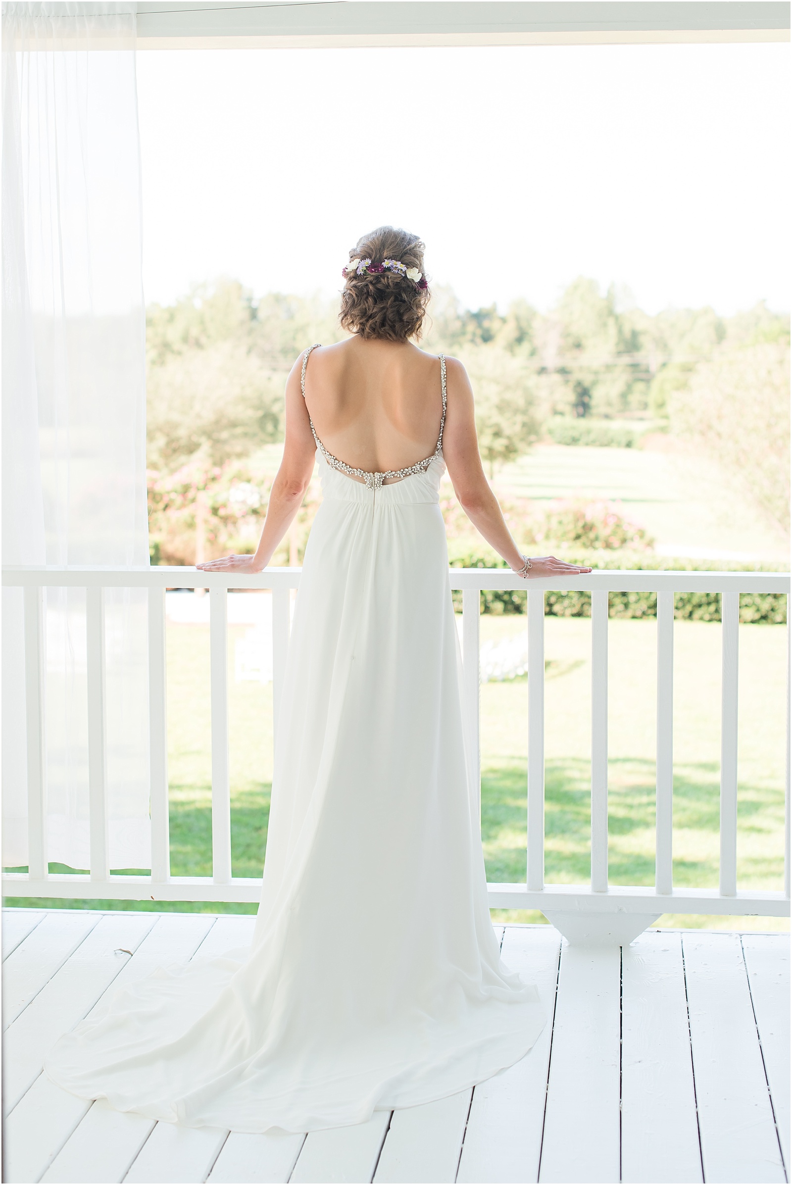 bride wearing white dress with sliver beaded straps looking out over the porch onto the ceremony site at Merry Hill Weddings