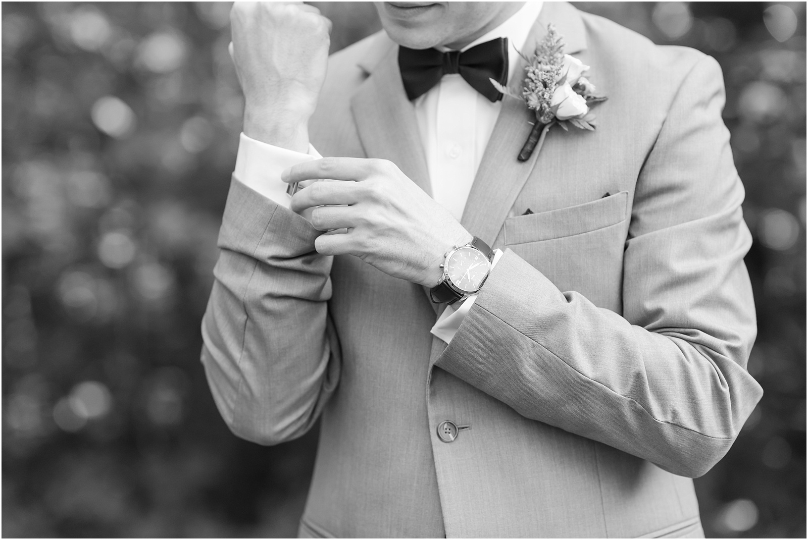 a black and white photograph of a groom fixing his cufflinks