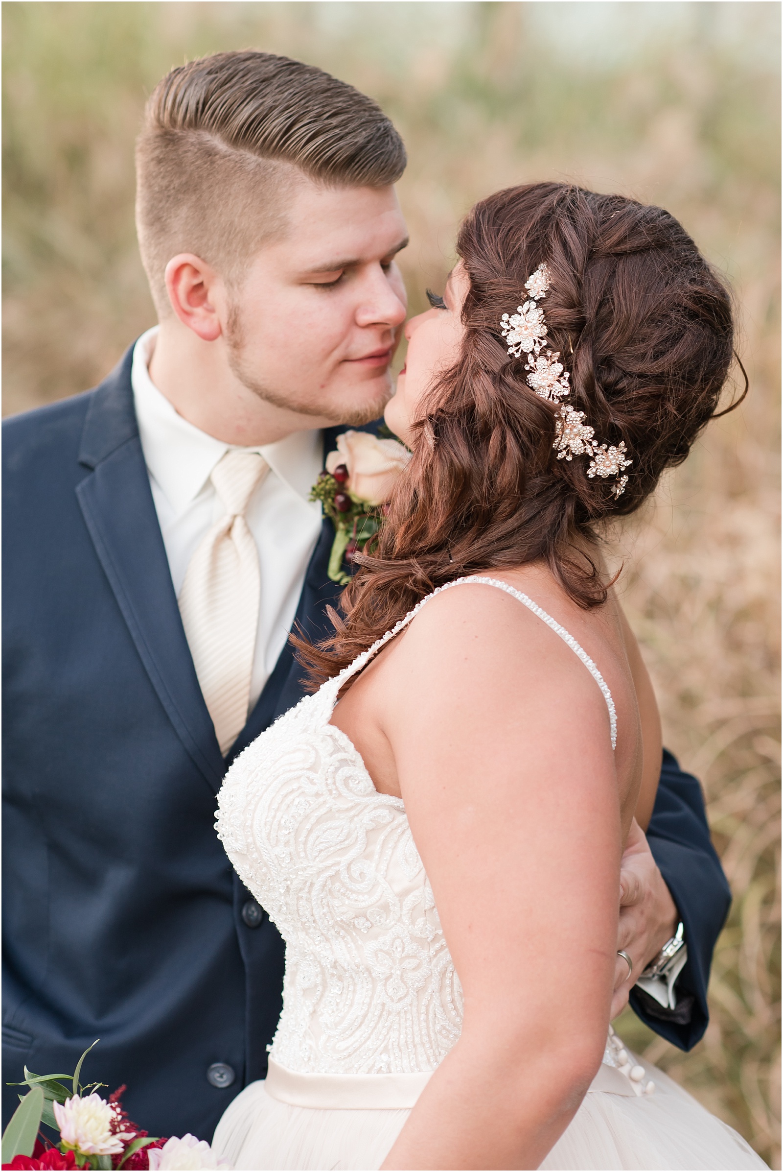 bride wearing champagne colored dress holding onto groom wearing a navy blue suit with cream colored tiealmost kissing in front of hayfield at Sedgefield Country Club