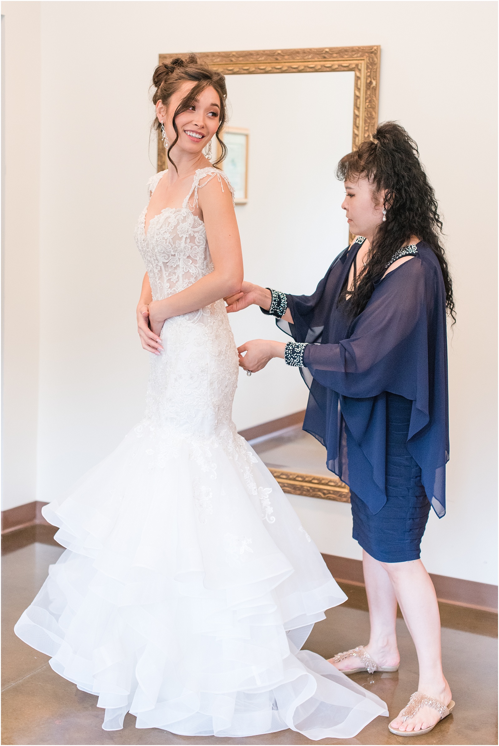mother in blue dress zipping up bride in her wedding dress