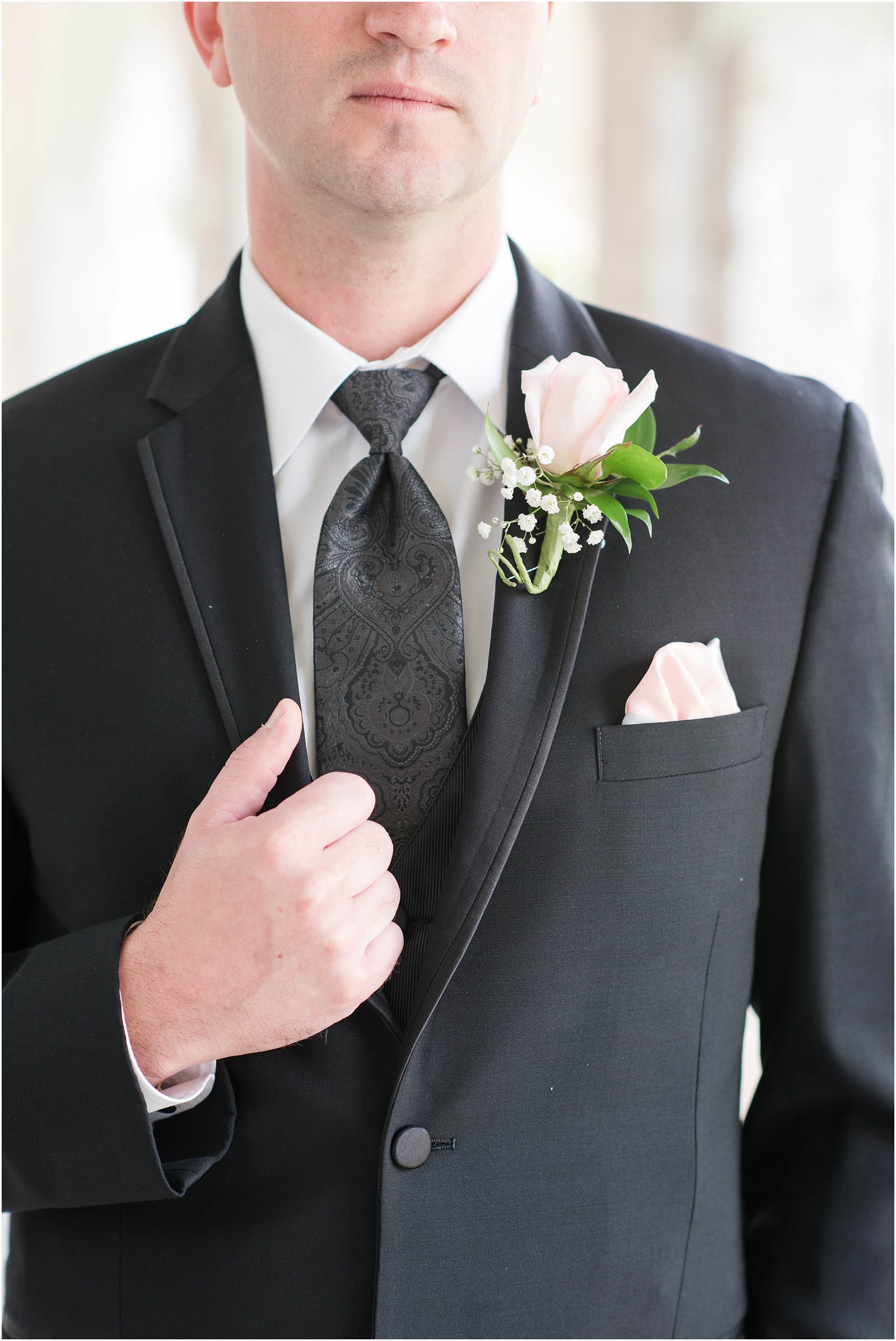 groom holding on to black suite jacket with pink flower 