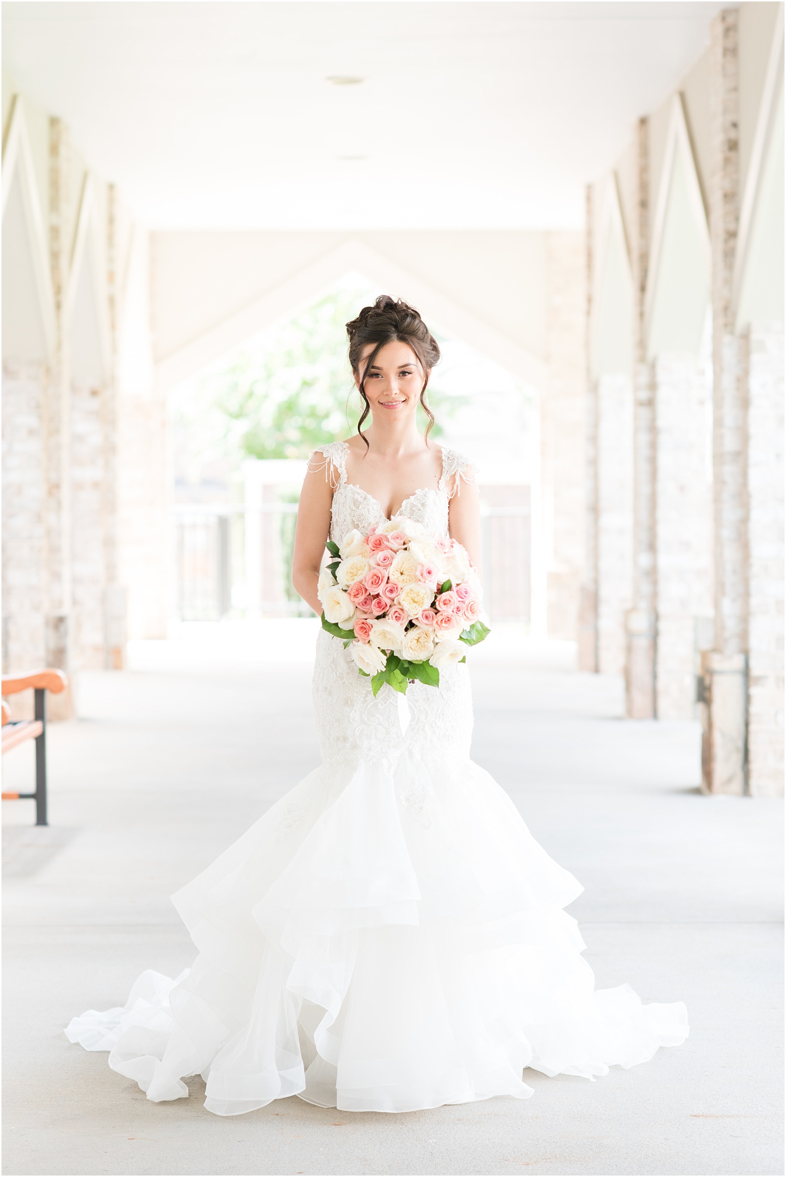 bride wearing couture bridal gown holding pink and white bouquet smiling at the camera