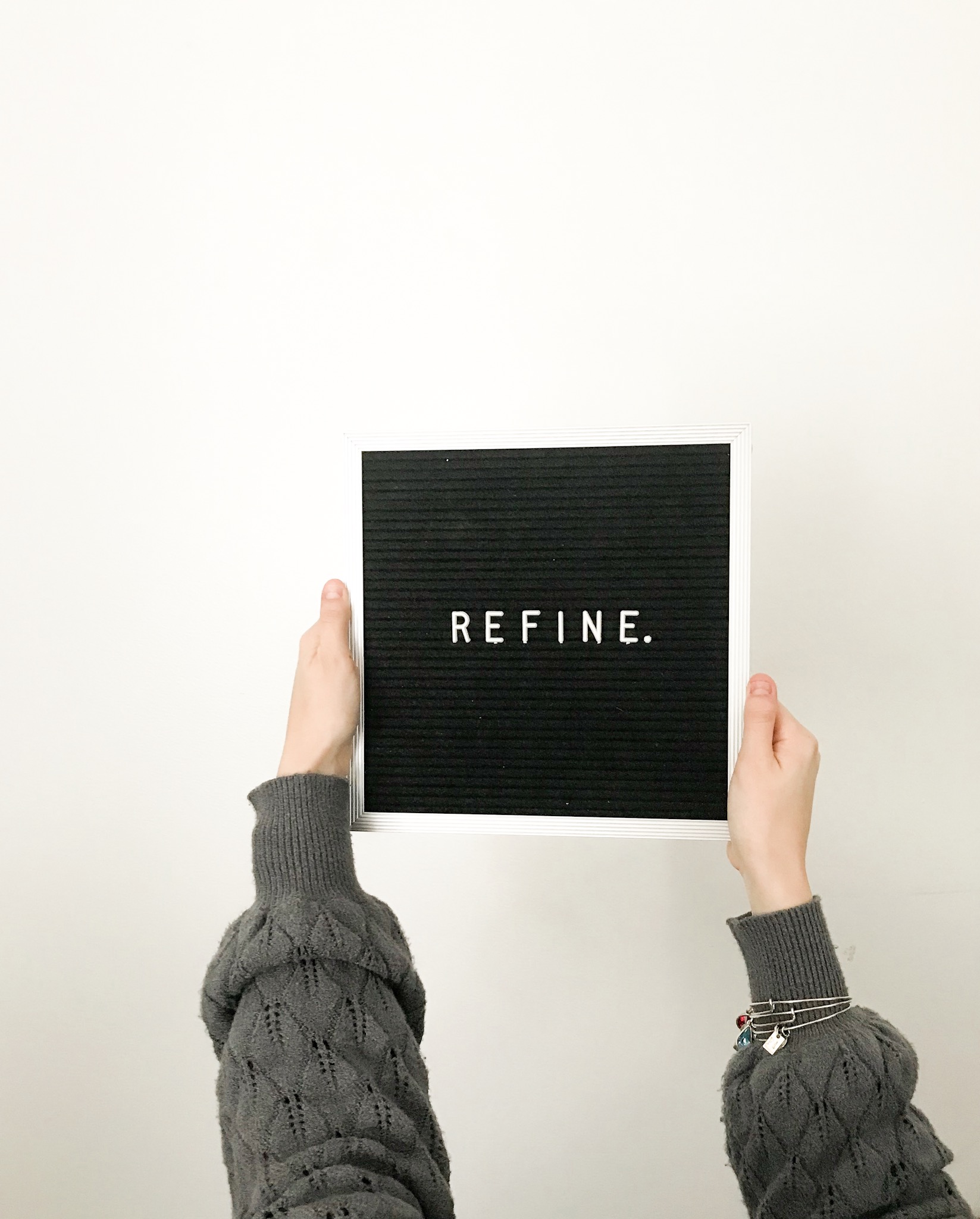 a young woman holding up a letterfolk small sliverframed letter board with the word refine for 2019 goal blog post